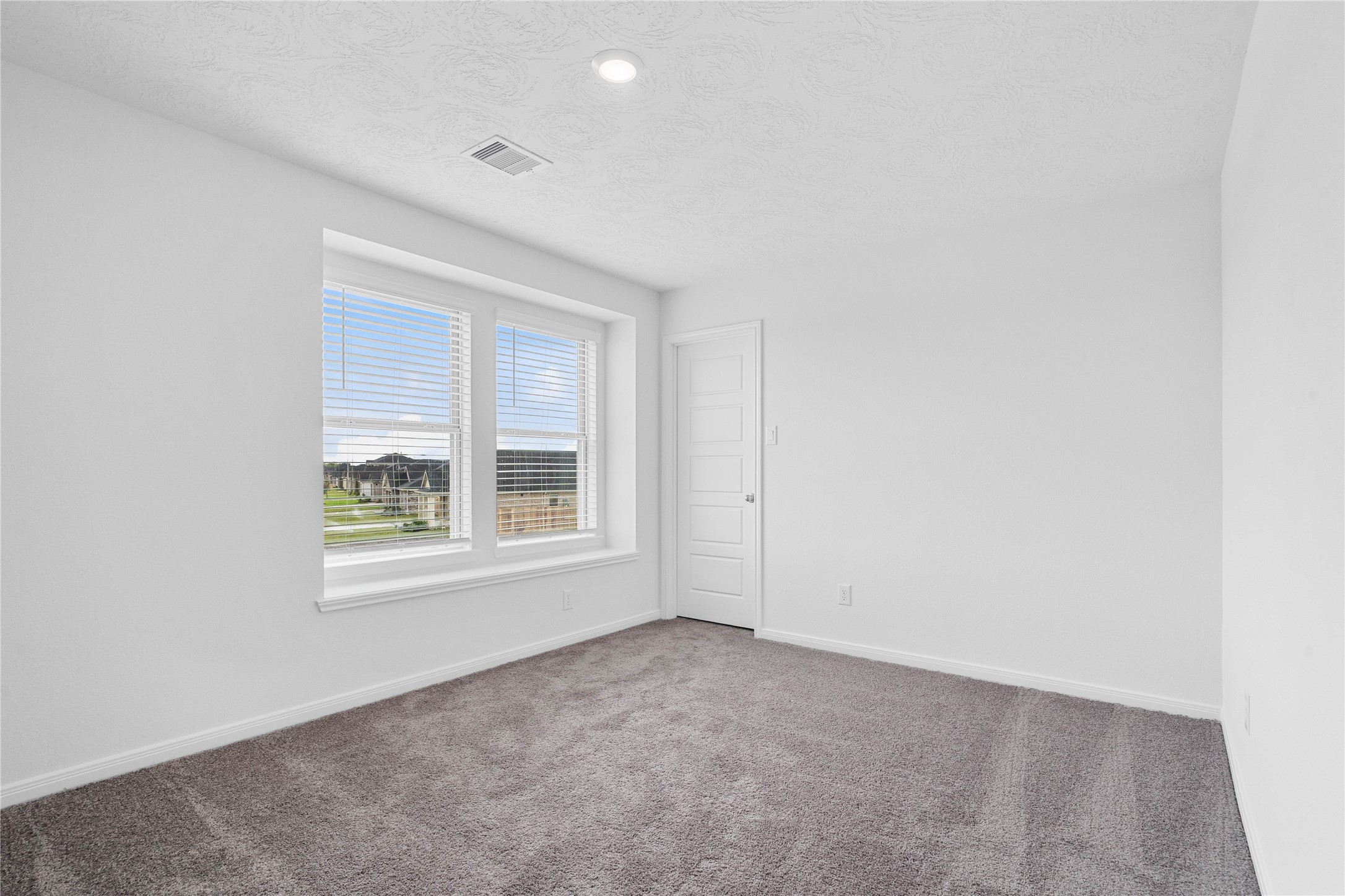 This secondary bedroom offers comfort and style with plush carpeting, neutral paint tones, recessed lighting, large windows with blinds, and a walk-in closet.