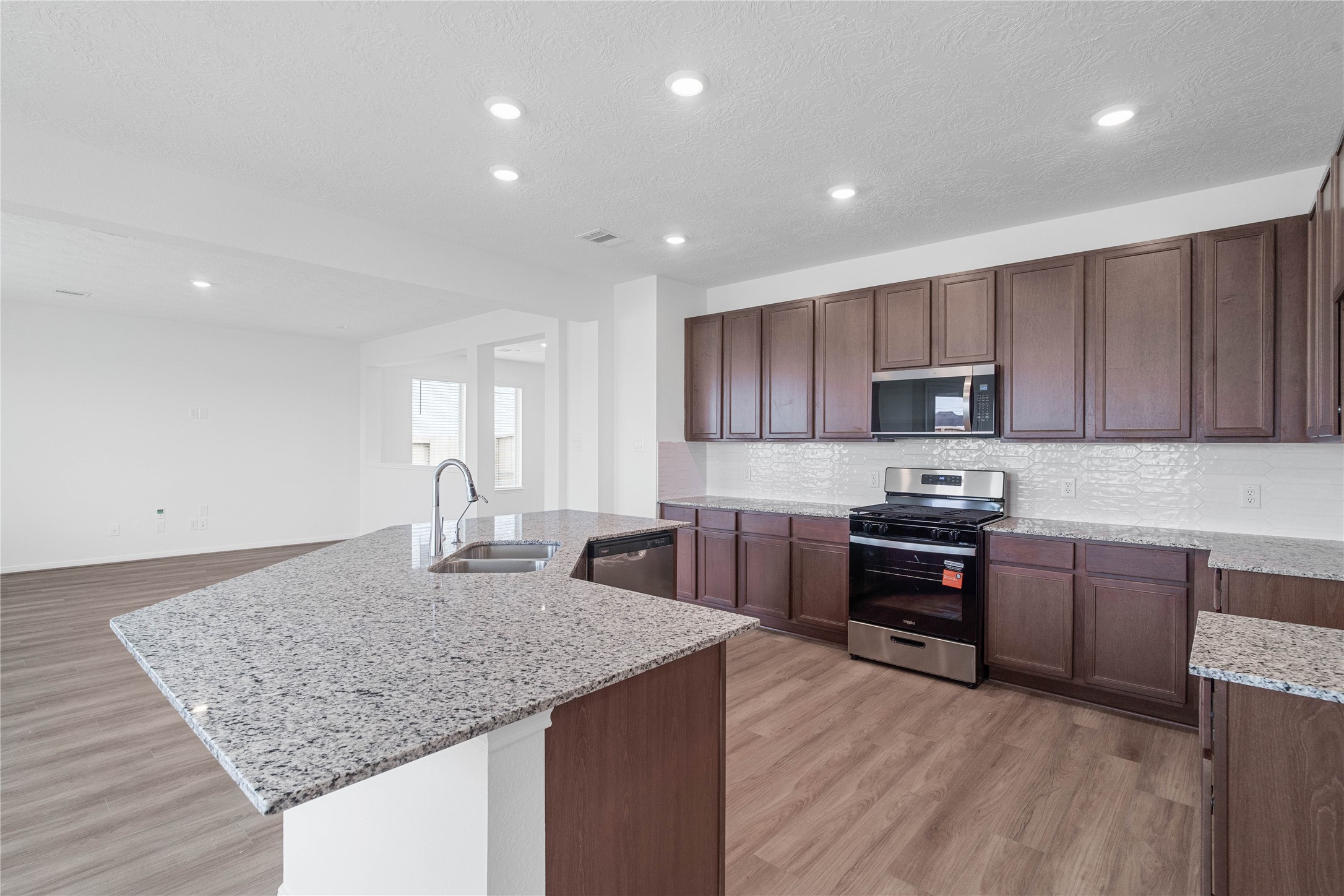 This spacious kitchen boasts soaring ceilings, Woodmont cabinets, granite countertops, stainless steel Whirlpool appliances, a modern Daltile backsplash, recessed lighting, an extended breakfast bar countertop, and a pantryall overlooking the expansive family room and breakfast nook.