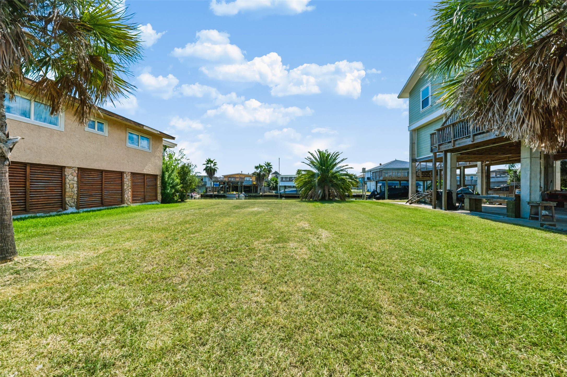 Looking across the lot toward the neighbor's raised home. This gives you a feel for scale and how the homes along here sit with living space up top and parking below. Build the same way and you would have canal views from every room up high.