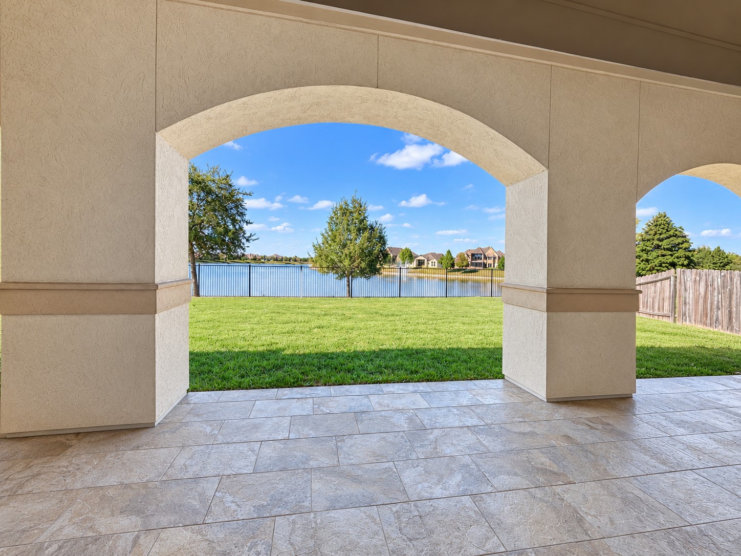 Inviting covered patio featuring arched openings and peaceful views of the backyard and lake.
