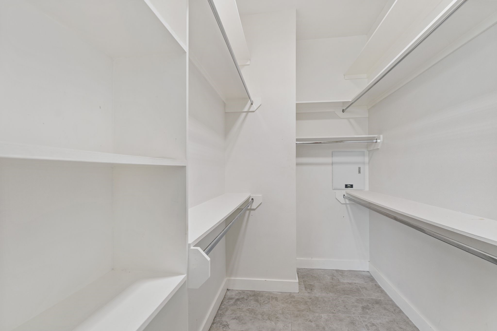 Spacious primary walk-in closet with built-in shelving and hanging rods along multiple walls for convenient storage.