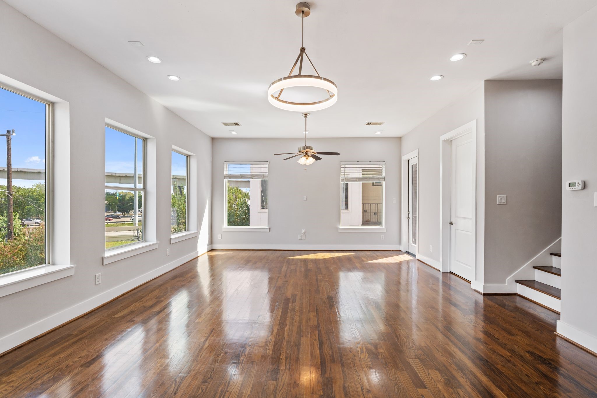 Bright living and dining area with large windows, modern light fixtures.