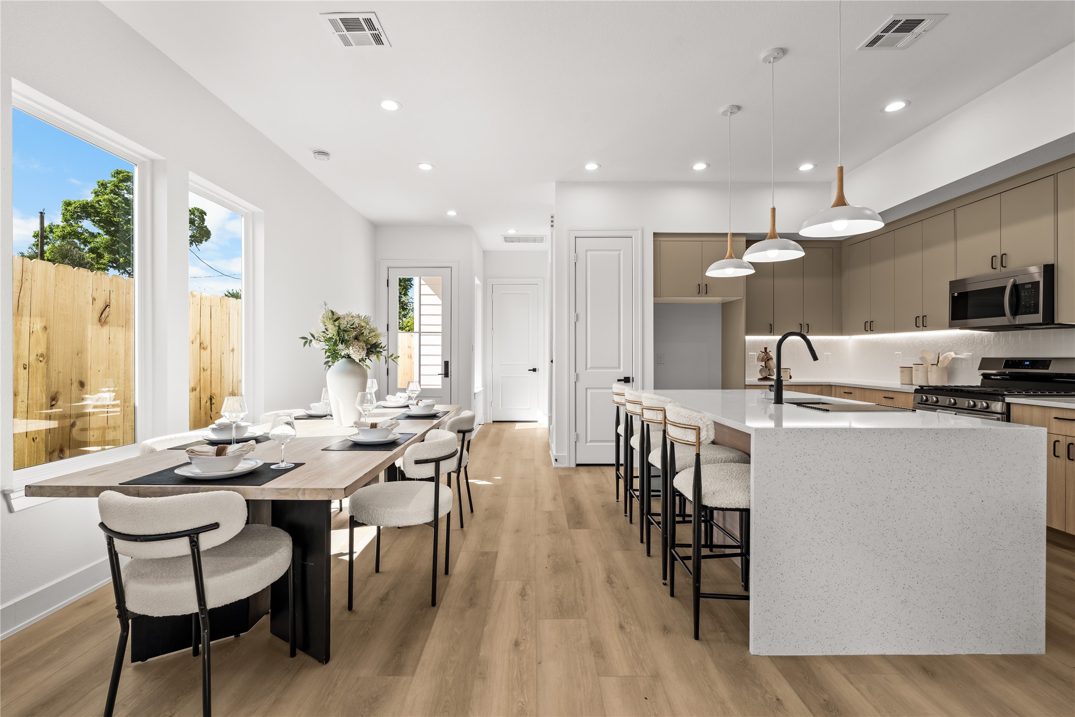 The main floor layout keeps everything open and connected. Light flooring and white walls maximize the natural light throughout the entire space. From the dining area, you have a direct view of the kitchen, which features a breakfast bar with seating and modern pendant lighting.