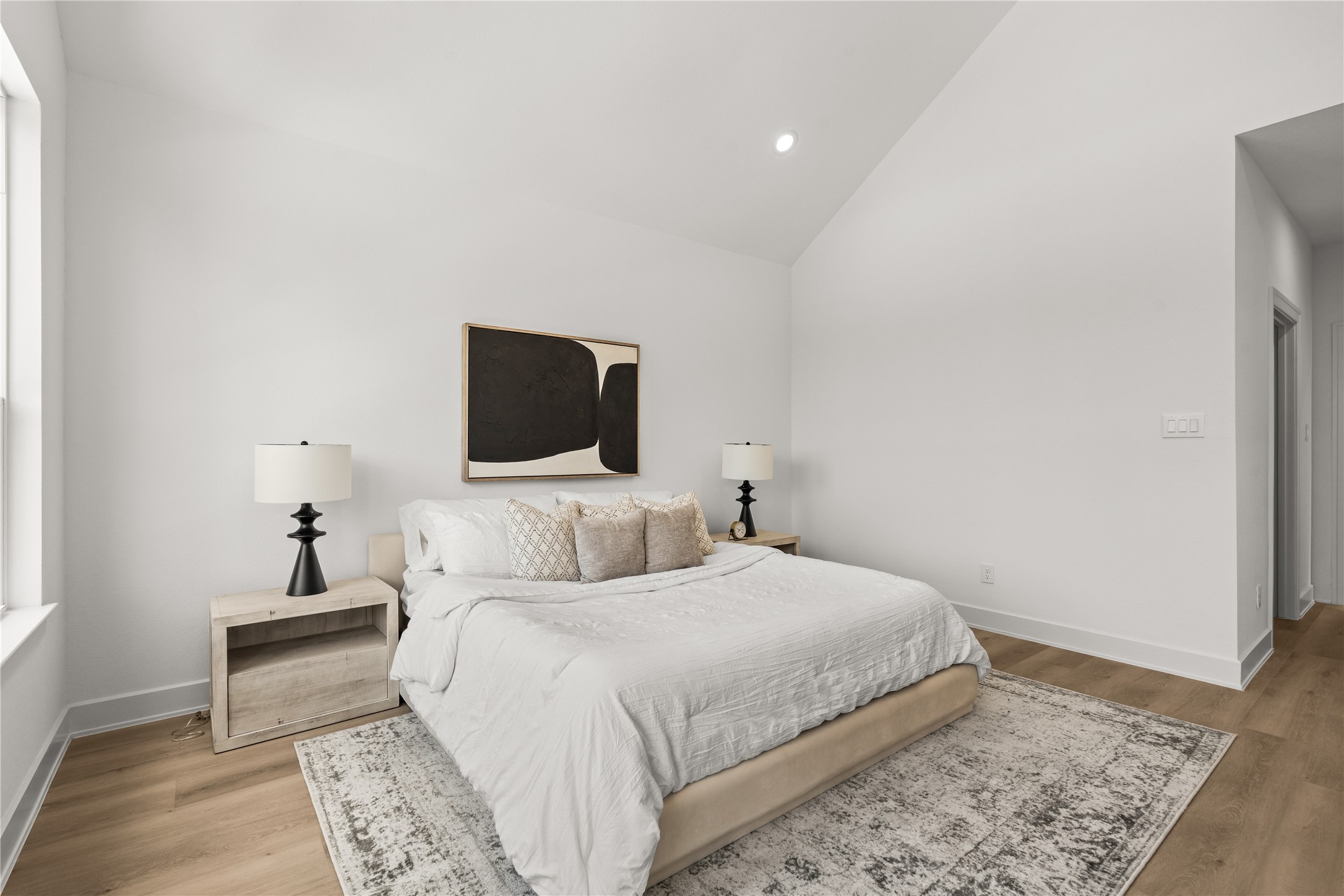 This view of the primary suite shows off its balanced layout, high vaulted ceiling, and smooth white walls.