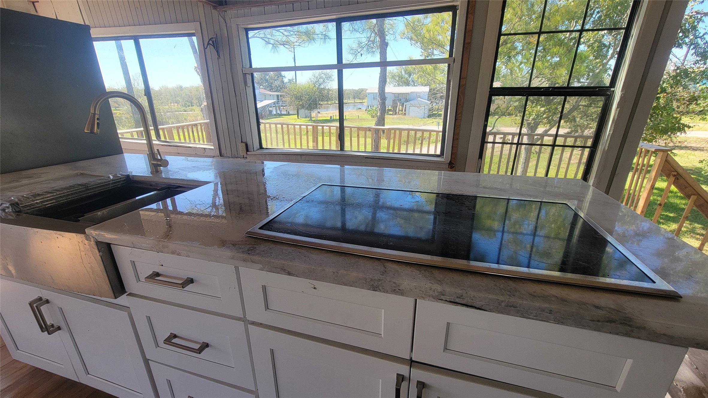 Bright kitchen with large windows showcasing scenic views. Features modern white cabinets, a sleek countertop with an integrated cooktop, and a stylish sink. Ideal for enjoying natural light and outdoor vistas.