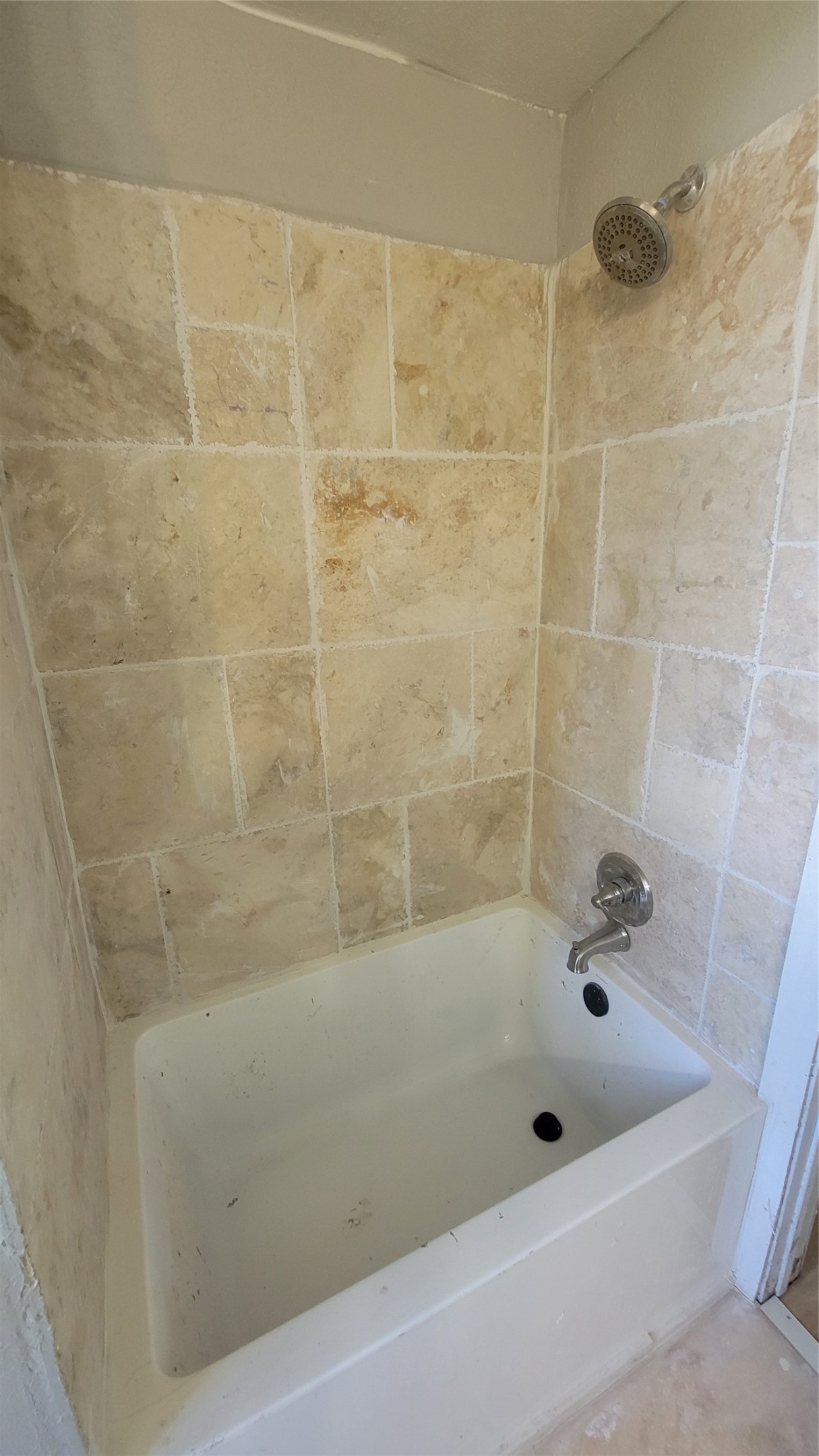 This photo shows a bathroom with a tub and shower combination. The walls are tiled in a neutral stone pattern, and the fixtures are silver-toned.