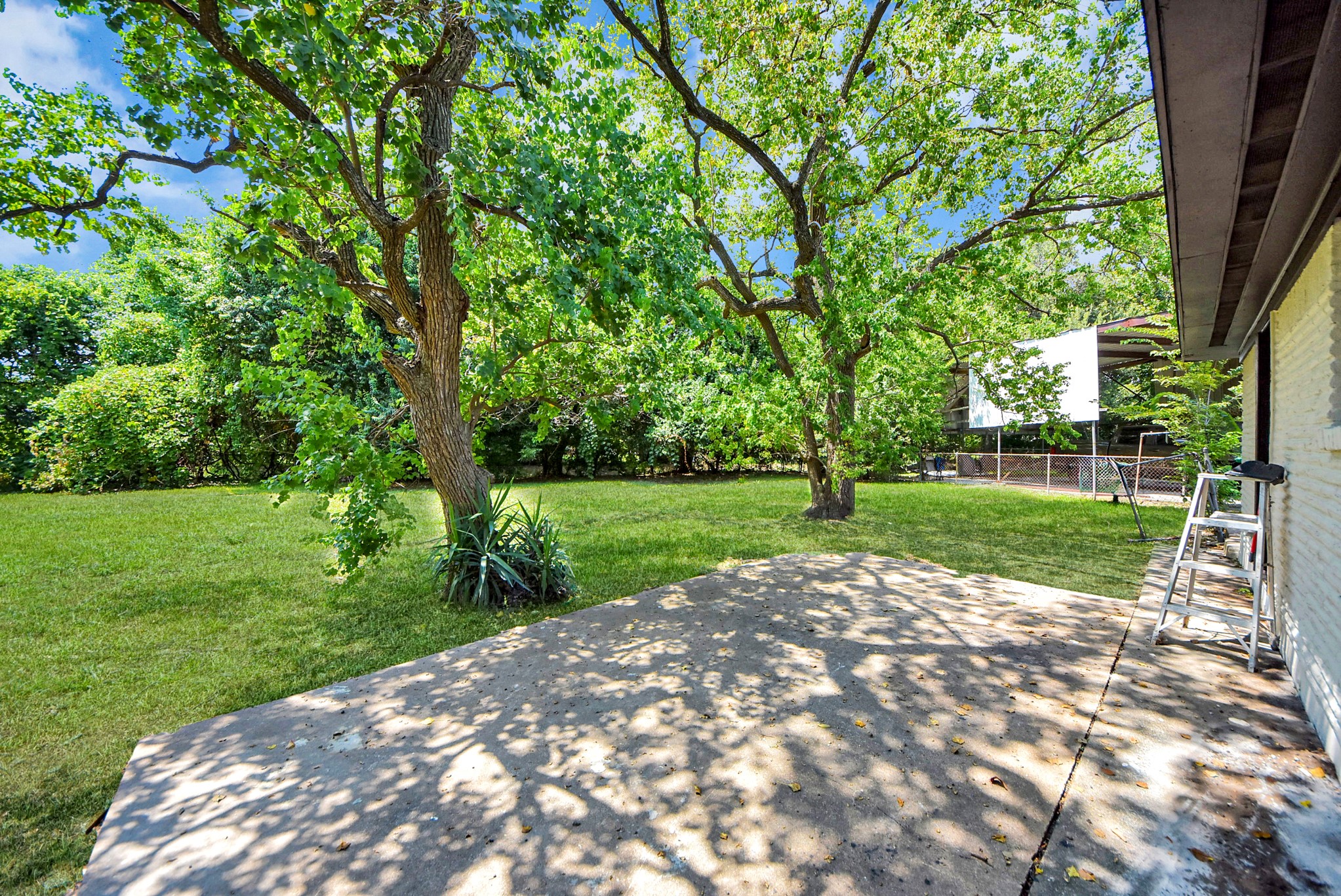 A spacious backyard with lush green grass and mature trees offers ample shade and a serene atmosphere, perfect for outdoor relaxation or entertaining.