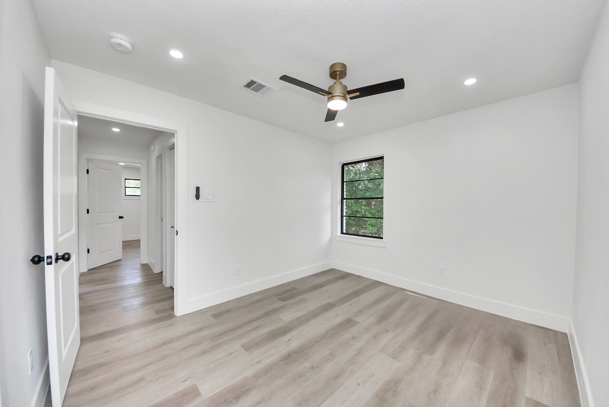 Bright and airy bedroom featuring sleek hardwood floors, a modern ceiling fan, and ample natural light from the window.