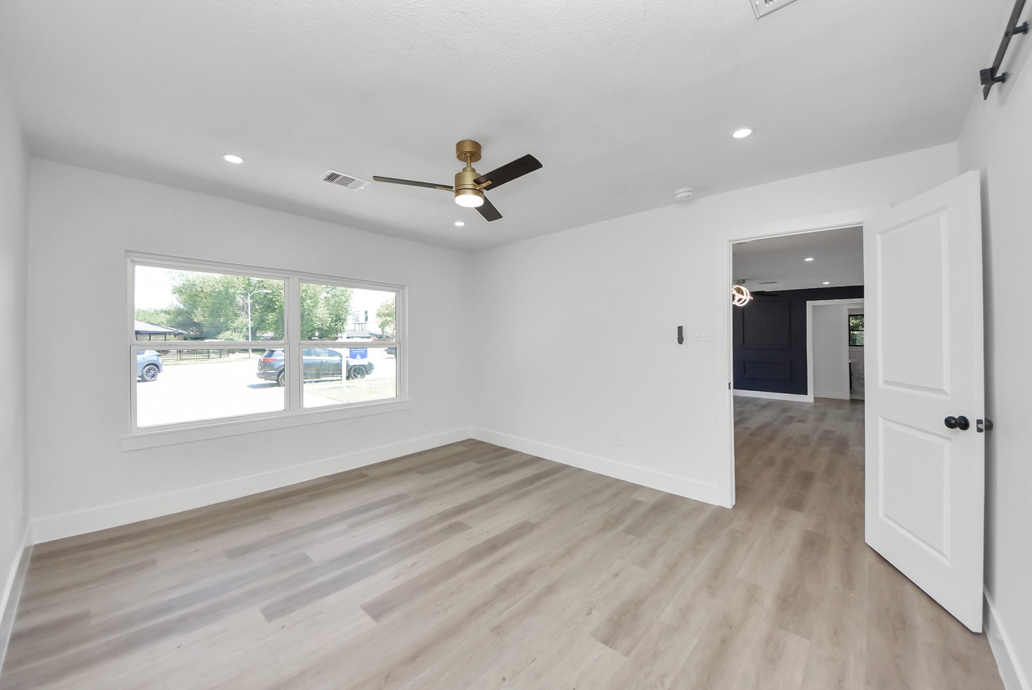 Bright and airy room featuring large windows, sleek flooring, and a modern ceiling fan, offering a seamless transition into the adjacent space.