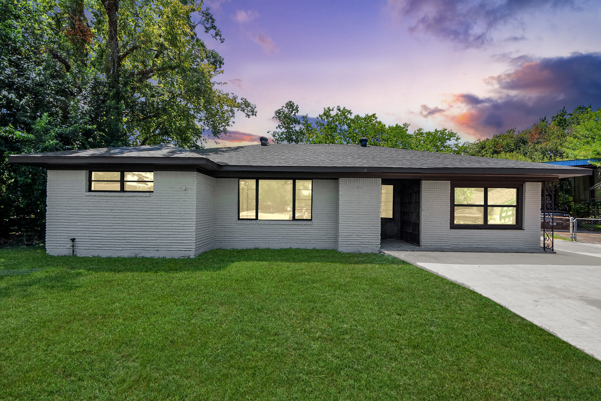 Charming single-story home with a fresh white brick exterior, large windows, and a spacious front yard framed by mature trees.