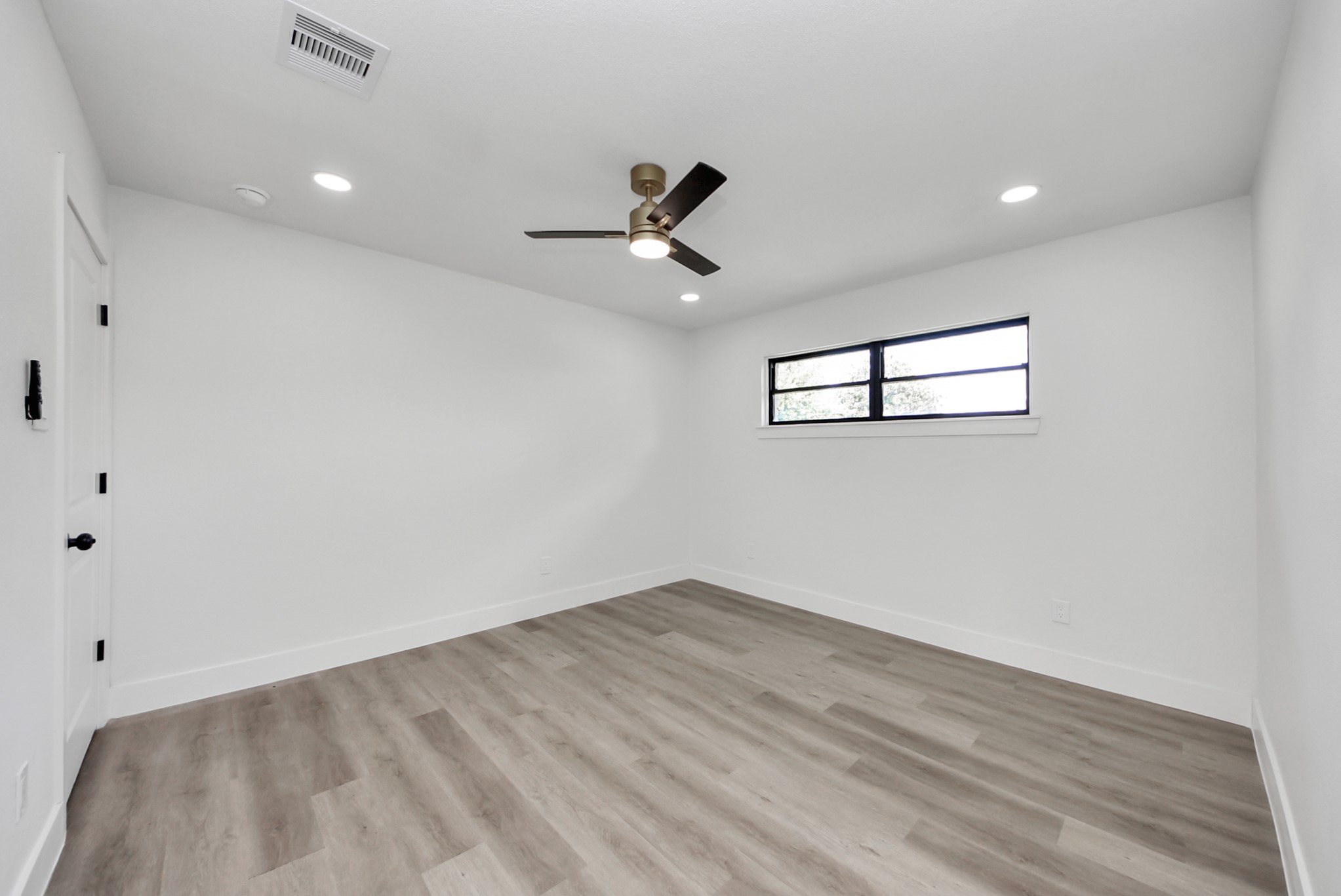 Spacious bedroom with sleek wood flooring, contemporary ceiling fan, and a large window offering ample natural light.