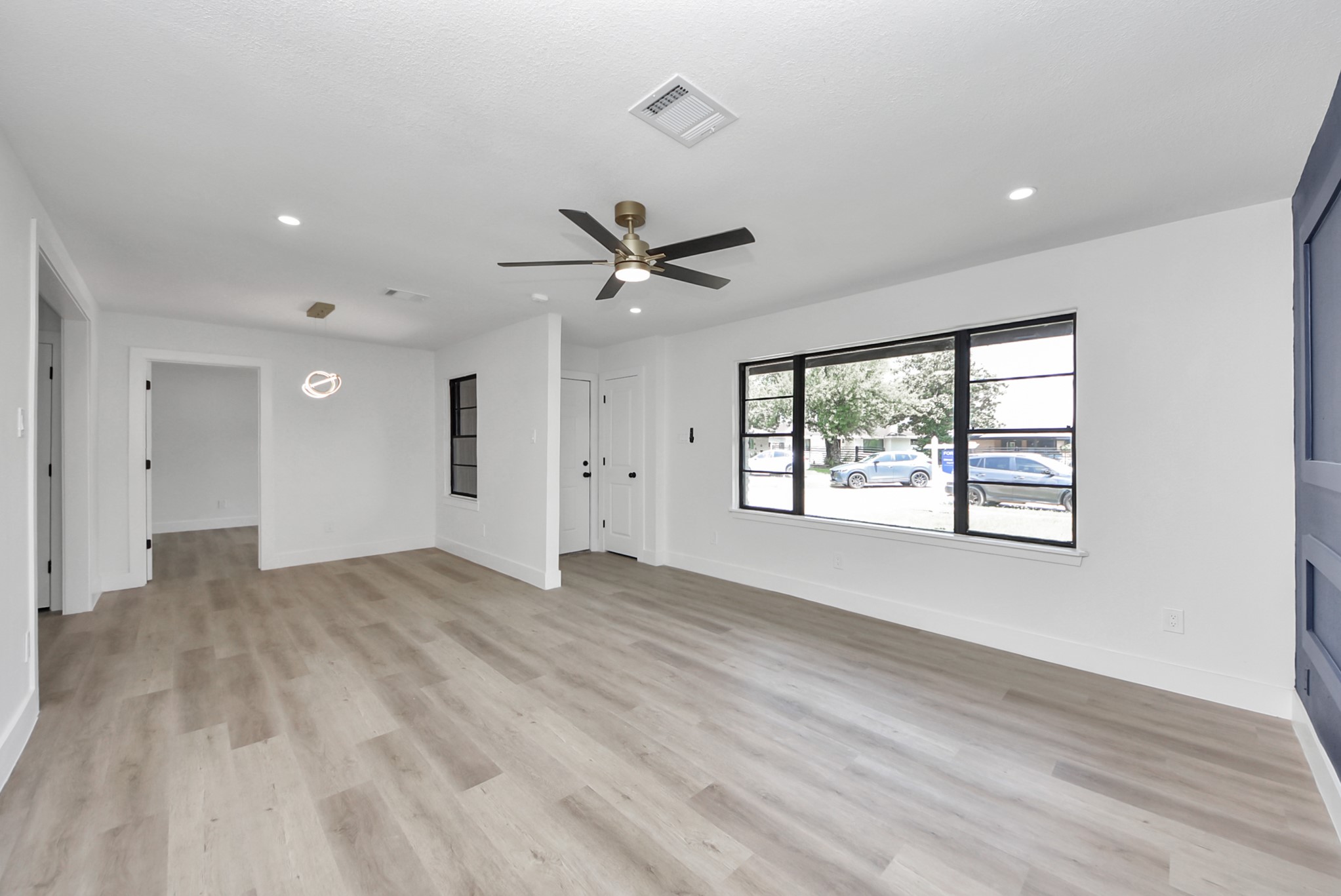 Bright and spacious living area with sleek laminate flooring, modern ceiling fan, and large windows offering abundant natural light.