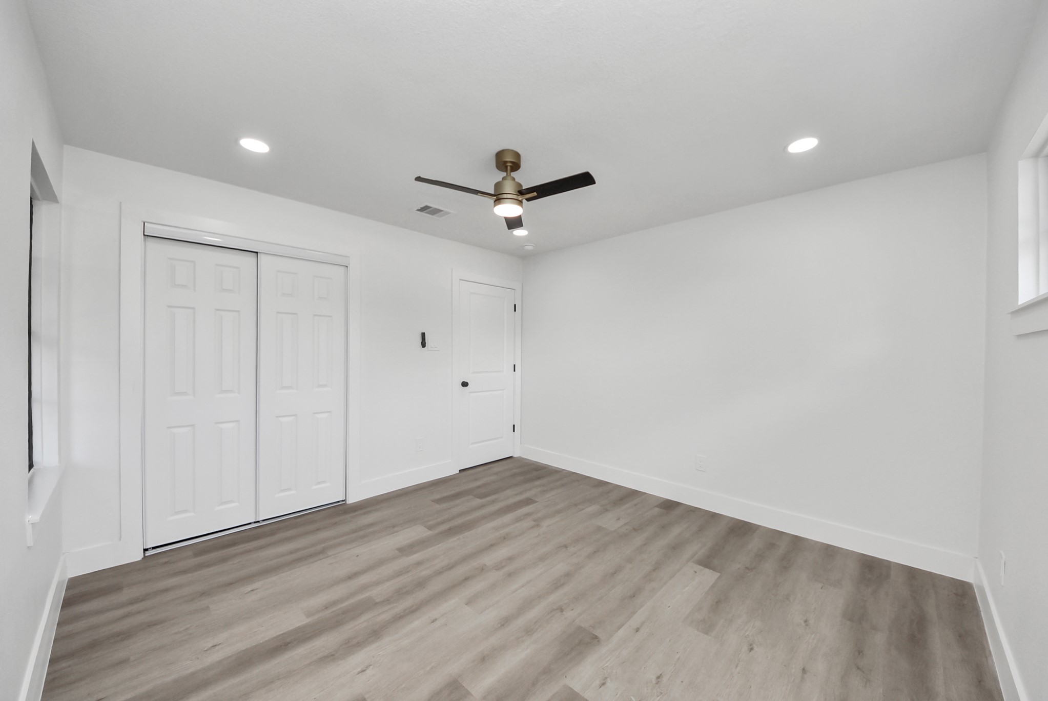 Bright and spacious room featuring modern recessed lighting, sleek ceiling fan, and stylish wood-look flooring, complemented by a large closet with sliding doors.