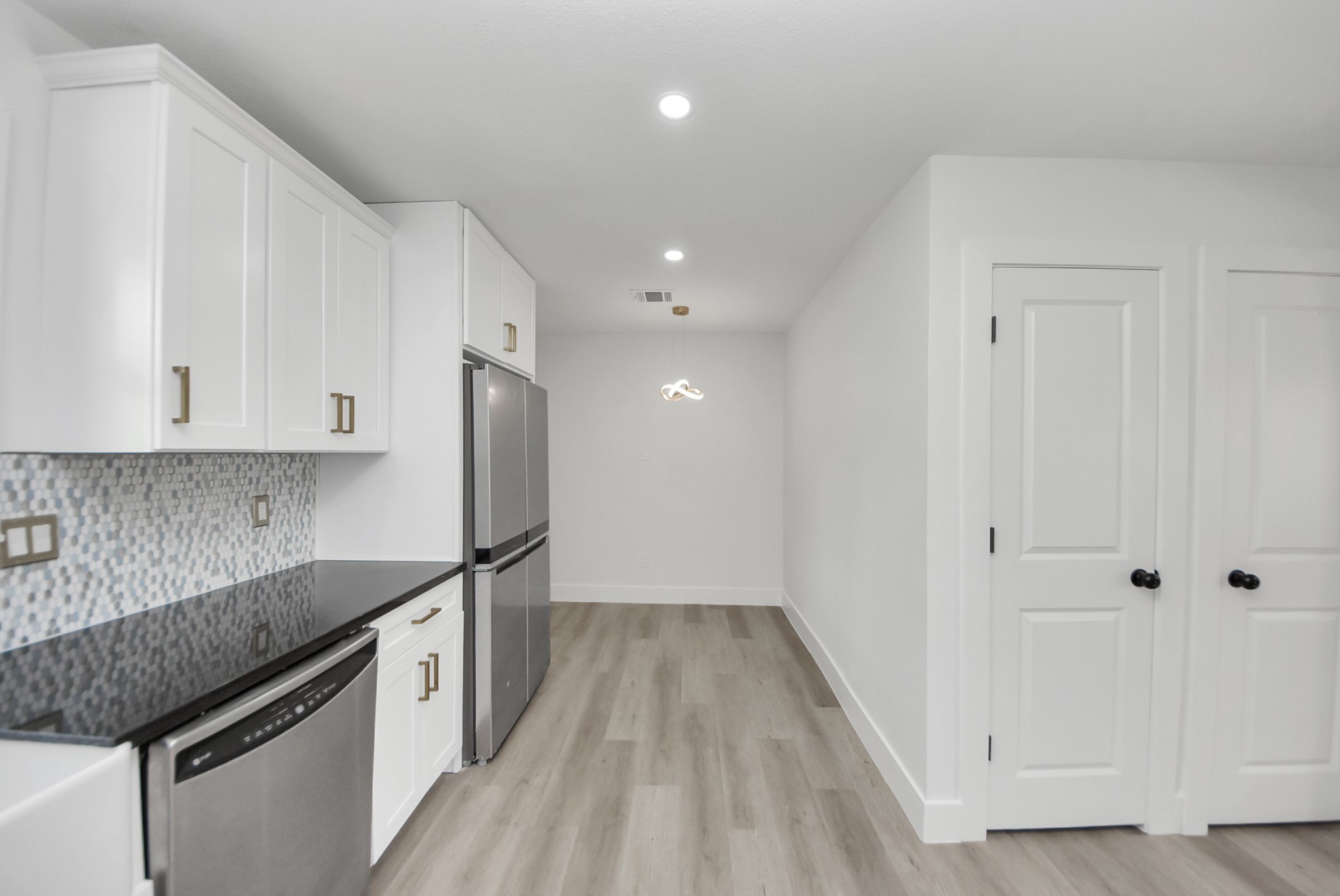 Modern kitchen with sleek white cabinetry, stainless steel appliances, and elegant black countertops, complemented by a stylish mosaic backsplash and chic lighting.