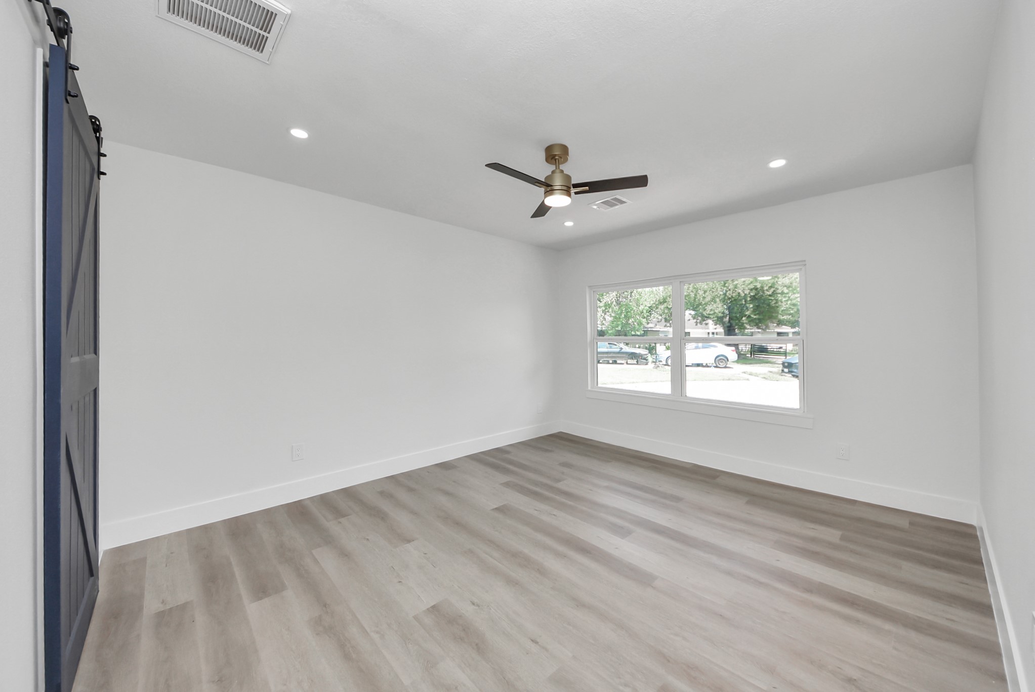 Bright, spacious room featuring sleek hardwood floors, a modern ceiling fan, and large windows that offer plenty of natural light.