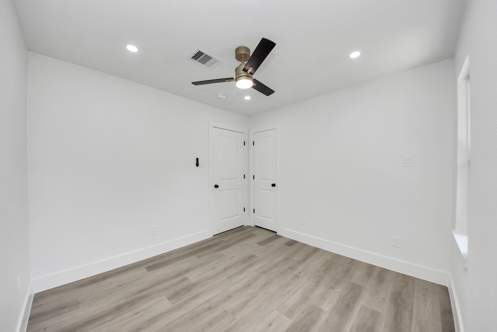 Bright, minimalist bedroom featuring sleek wood flooring, fresh white walls, and a modern ceiling fan, offering a serene and contemporary space.