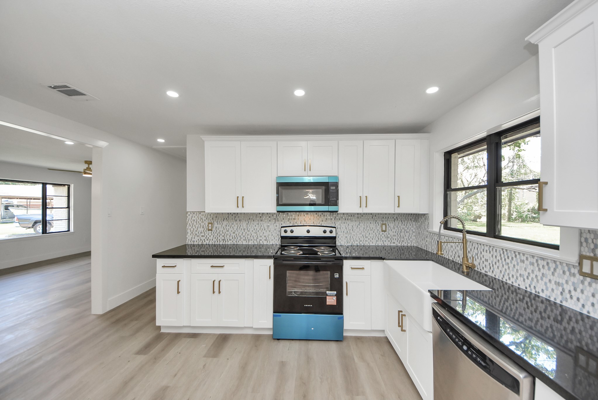 Sleek and modern kitchen featuring stainless steel appliances, elegant white cabinetry, and a stylish mosaic backsplash, complemented by a spacious farmhouse sink and ample natural light from large windows.