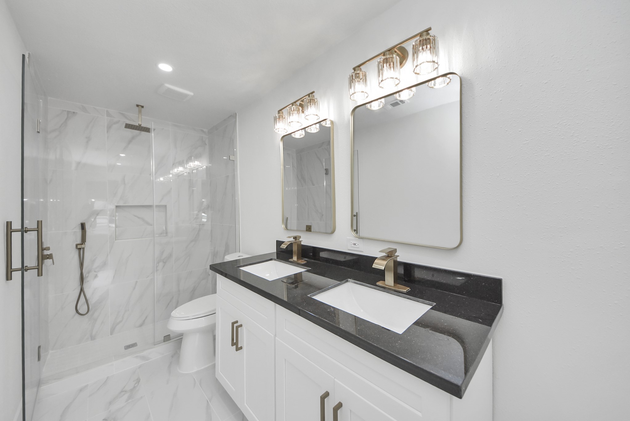 Elegant bathroom featuring a sleek double vanity with black countertops, gold fixtures, and a spacious glass-enclosed shower with modern tilework.