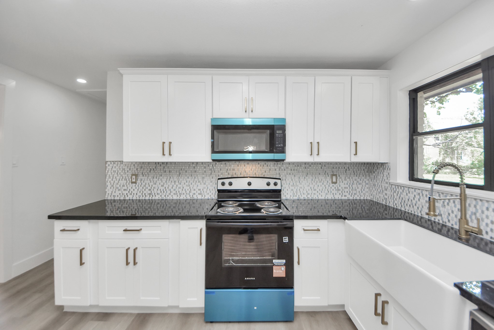 Sleek kitchen featuring modern appliances, crisp white cabinetry, and elegant black countertops, complemented by a stylish tile backsplash and a spacious farmhouse sink.