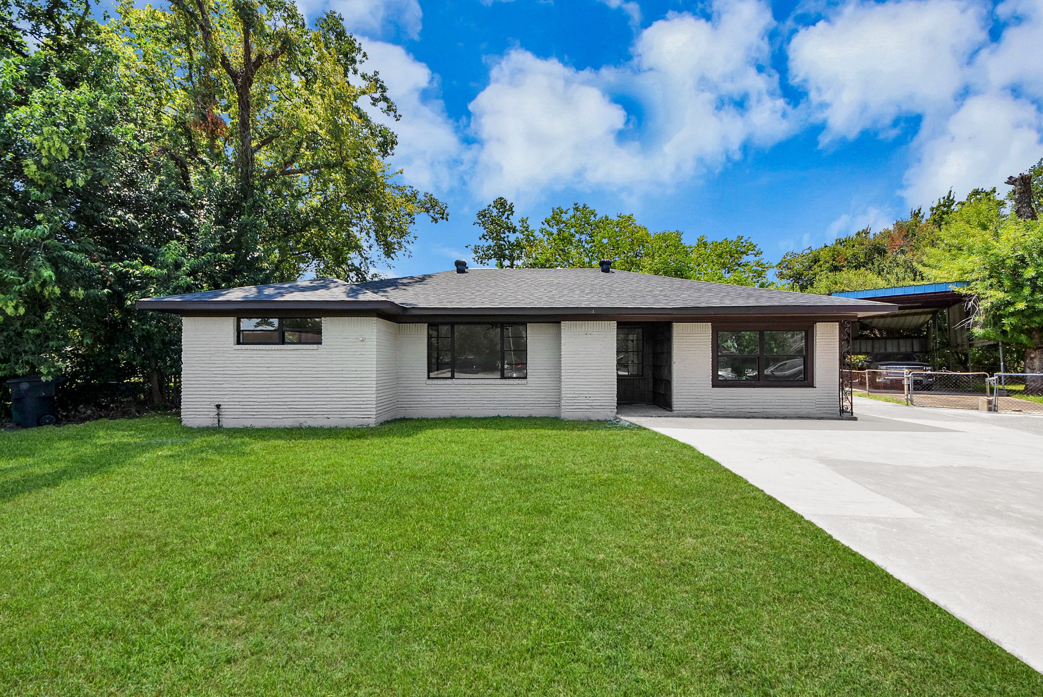 Charming single-story home with a sleek modern exterior, set amidst lush greenery and featuring a spacious front lawn and inviting driveway.