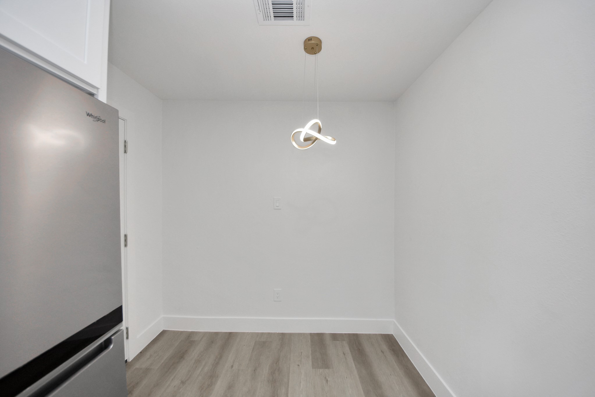 Chic and minimal dining area featuring modern light fixtures, sleek stainless steel appliances, and elegant wood flooring.