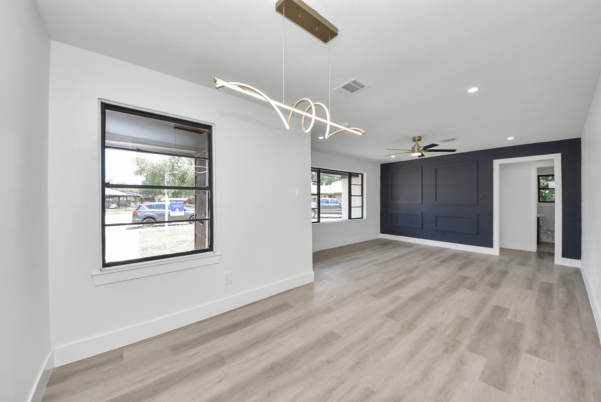 Spacious living area with modern lighting, sleek wood flooring, and a stylish accent wall, offering a contemporary and inviting atmosphere.