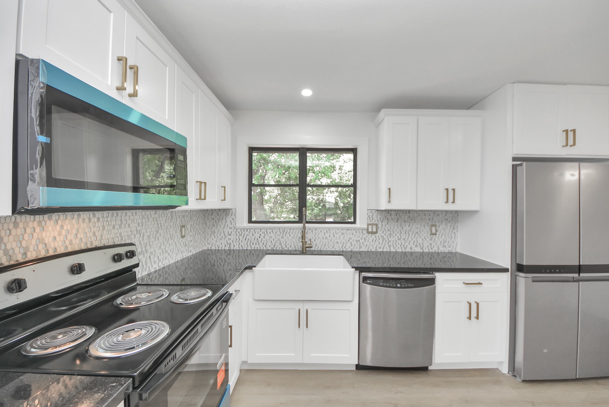 Charming kitchen with modern appliances, sleek black countertops, and a stylish farmhouse sink. Bright white cabinetry complements the mosaic tile backsplash, creating a fresh and inviting atmosphere.