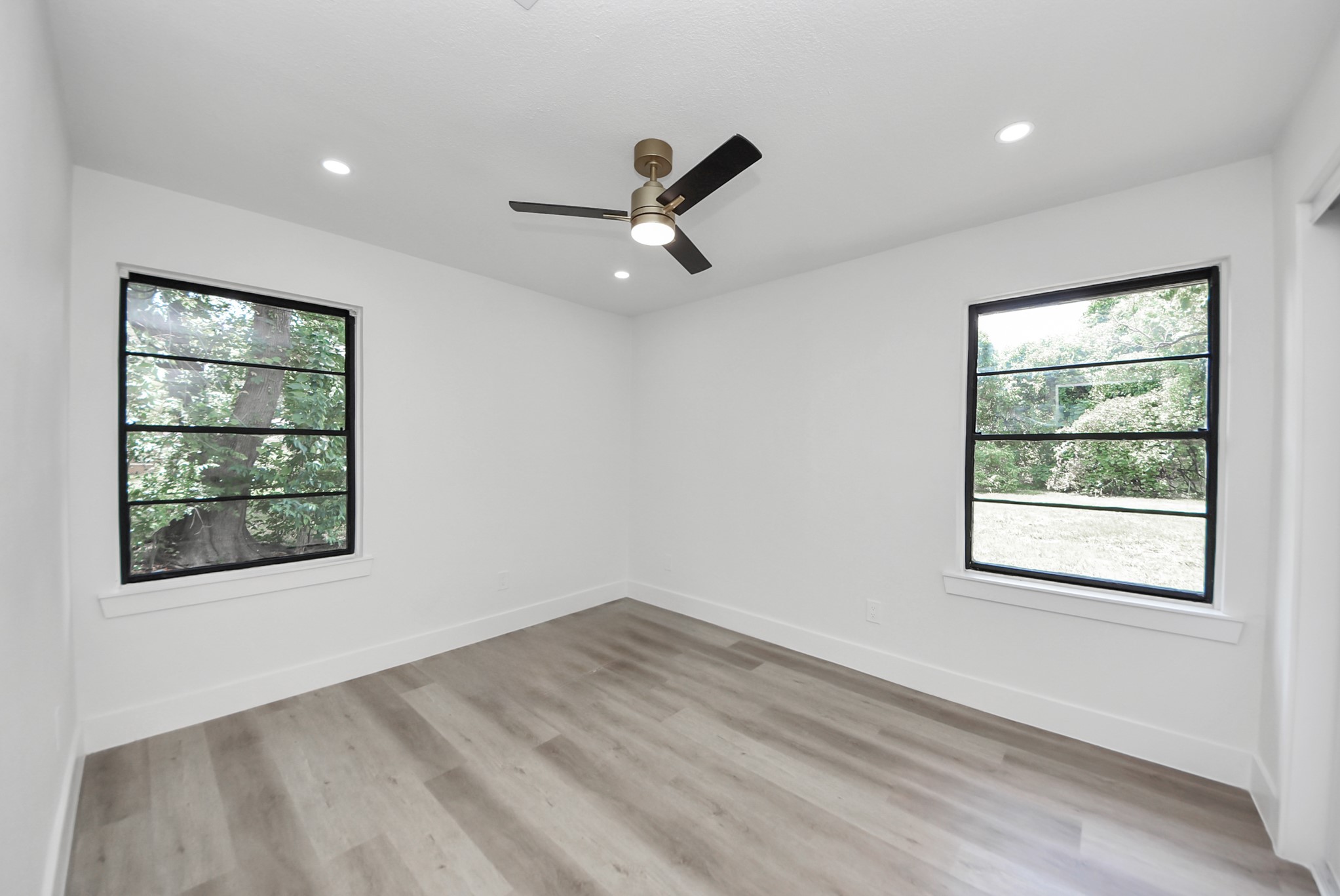 Bright and airy bedroom featuring large windows with tranquil views, sleek hardwood flooring, and a modern ceiling fan.