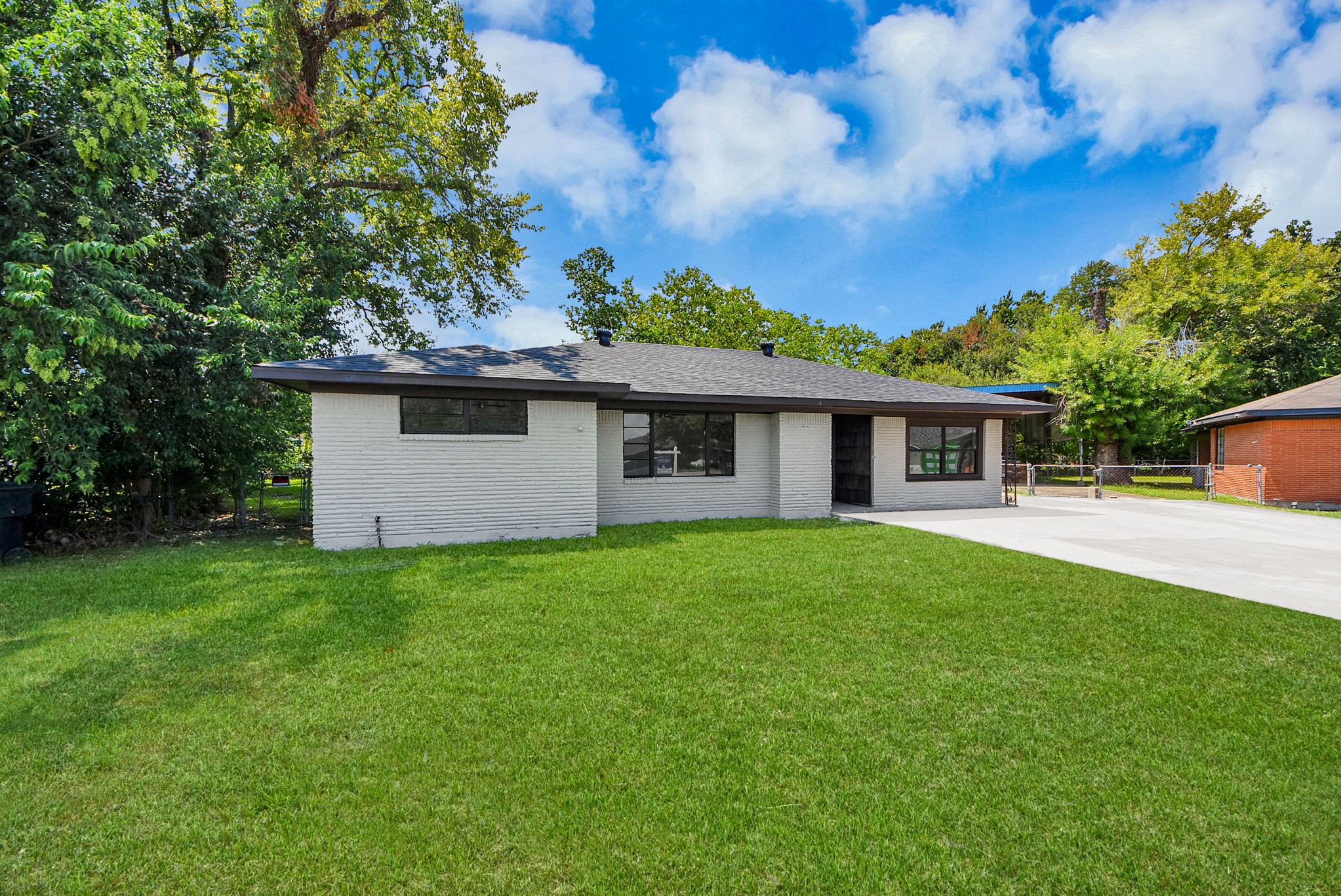 Charming brick ranch-style home with a spacious front yard and a sleek modern roof, surrounded by mature trees for added privacy and shade.