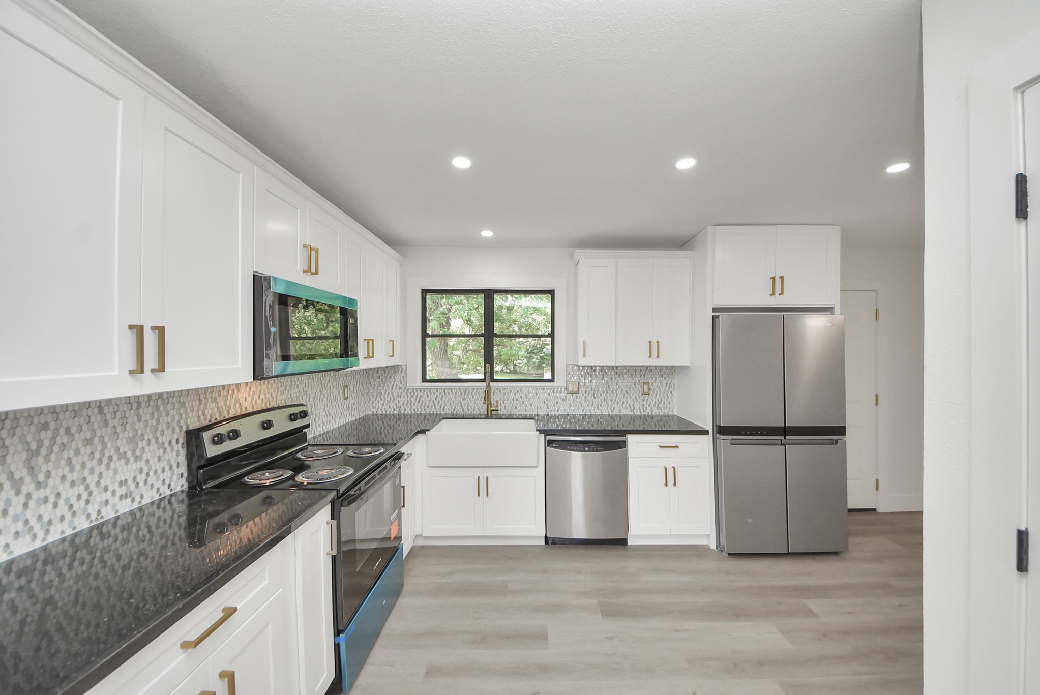 Modern kitchen featuring sleek white cabinetry, stainless steel appliances, and a stylish farmhouse sink. The elegant mosaic backsplash and dark countertops complement the bright, open space.