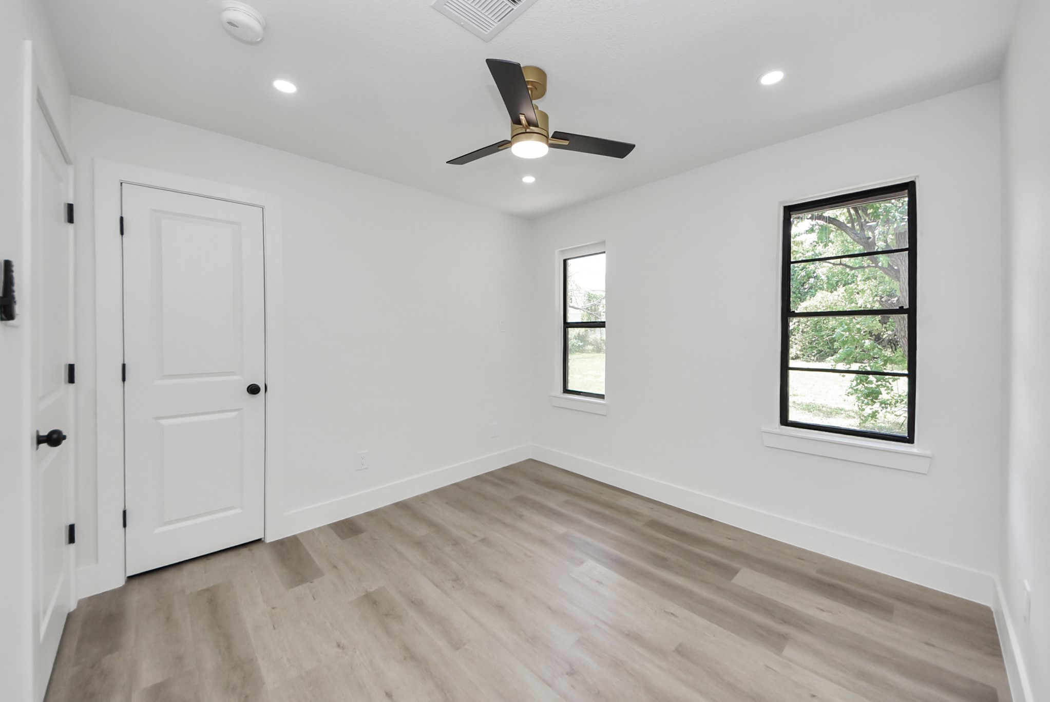 Bright and airy room featuring sleek hardwood floors, modern ceiling fan, and large windows offering abundant natural light.