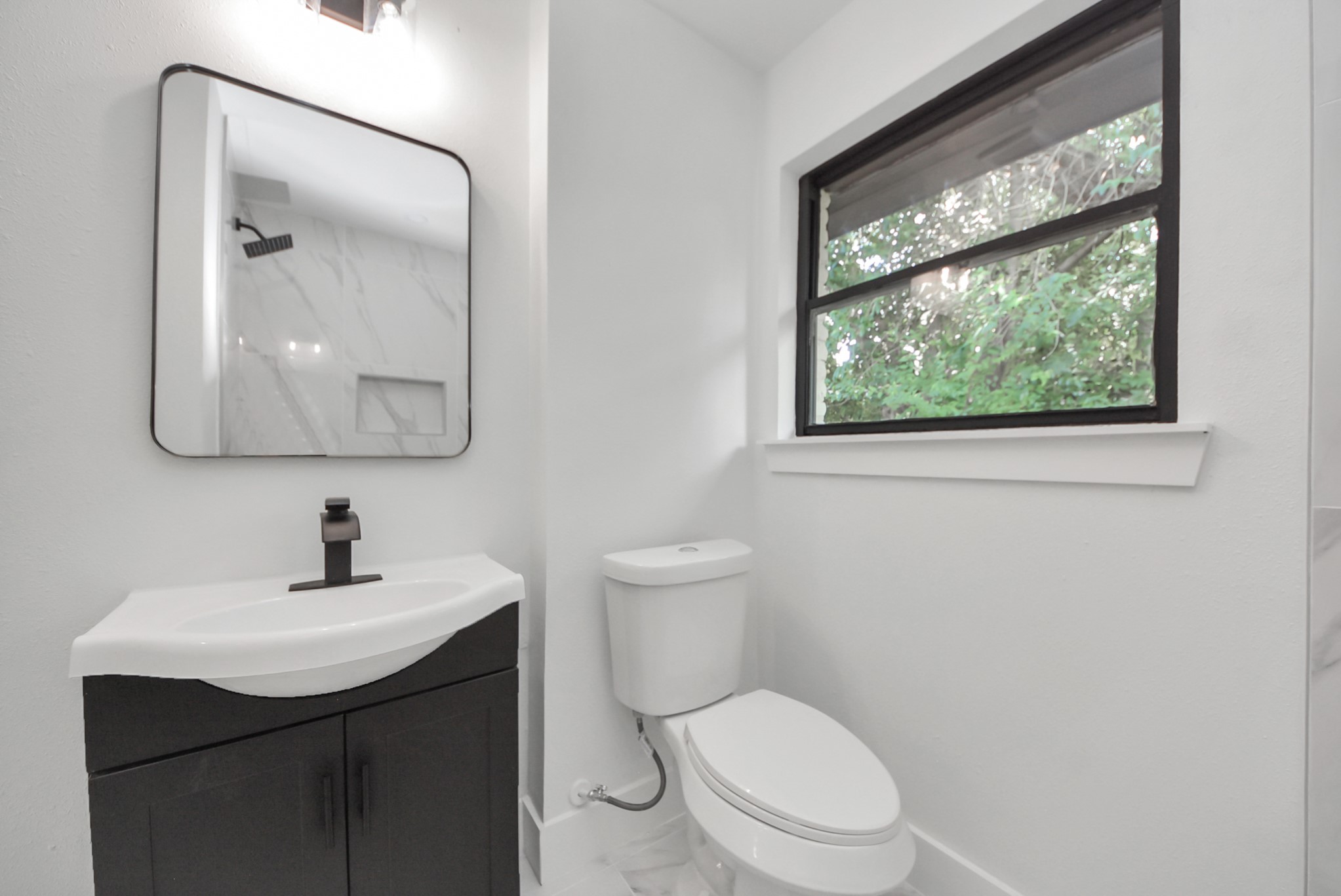 Bright, modern bathroom featuring a sleek vanity, stylish fixtures, and a large window with a serene view.