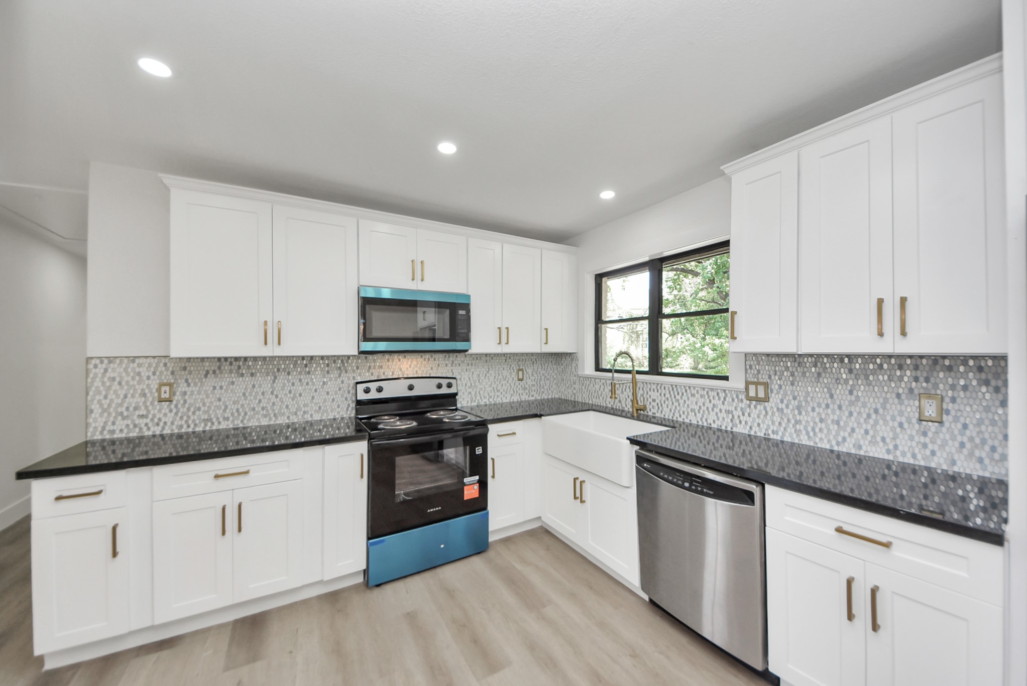 Modern kitchen featuring sleek black countertops, white cabinetry, and a stylish mosaic backsplash. Equipped with stainless steel appliances and a farmhouse sink, it offers both functionality and elegance.