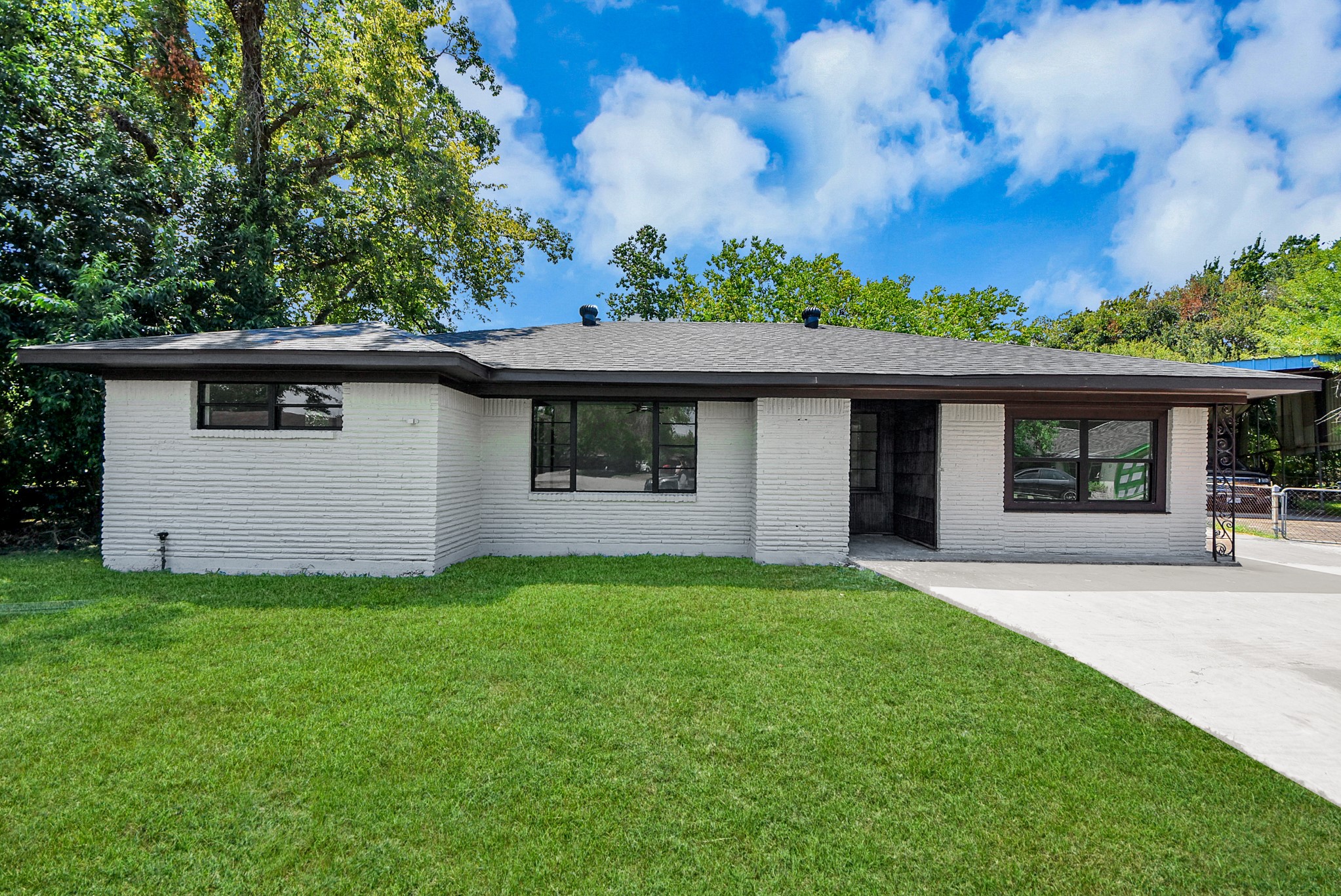 Charming single-story home with a modern exterior, featuring a sleek white brick facade and large windows for abundant natural light, set on a lush green lawn.