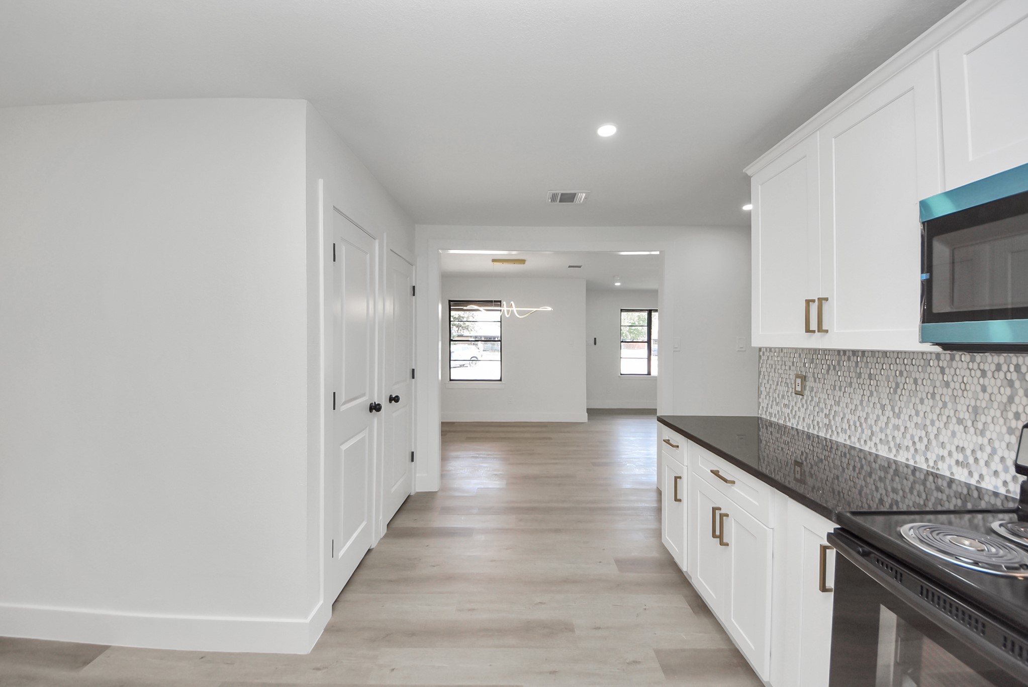 Modern kitchen with sleek white cabinetry, black countertops, and stylish backsplash leading into an open, well-lit living space.