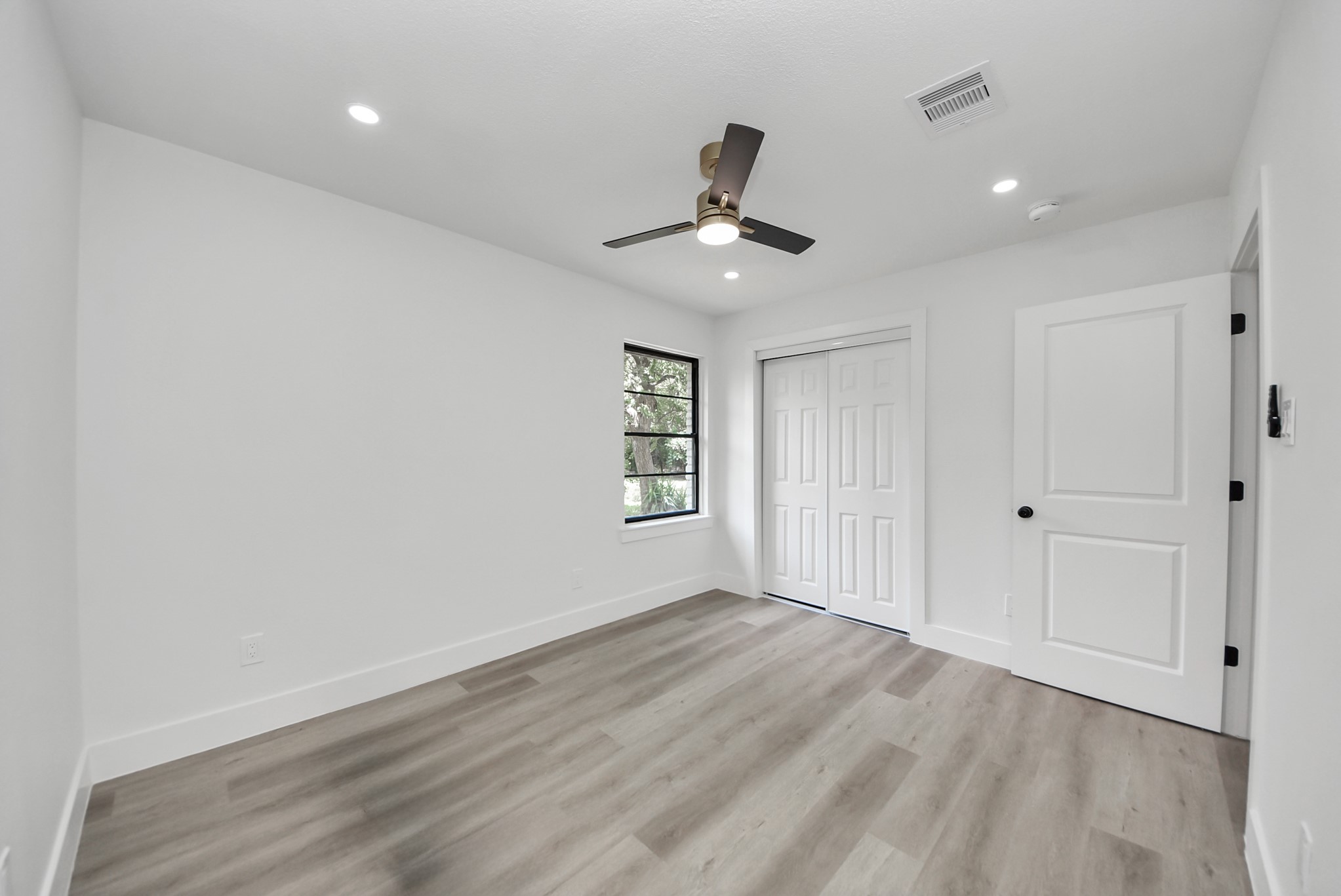 Bright and airy bedroom featuring sleek laminate flooring, a modern ceiling fan, and ample closet space, accentuated by soft recessed lighting.