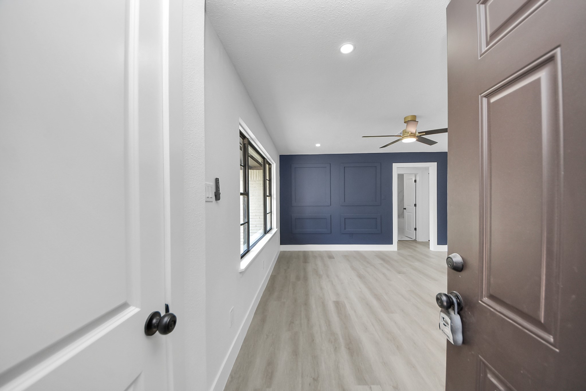 Bright and inviting room featuring a stylish blue accent wall, modern ceiling fan, and sleek wood flooring, offering a perfect blend of comfort and contemporary design.