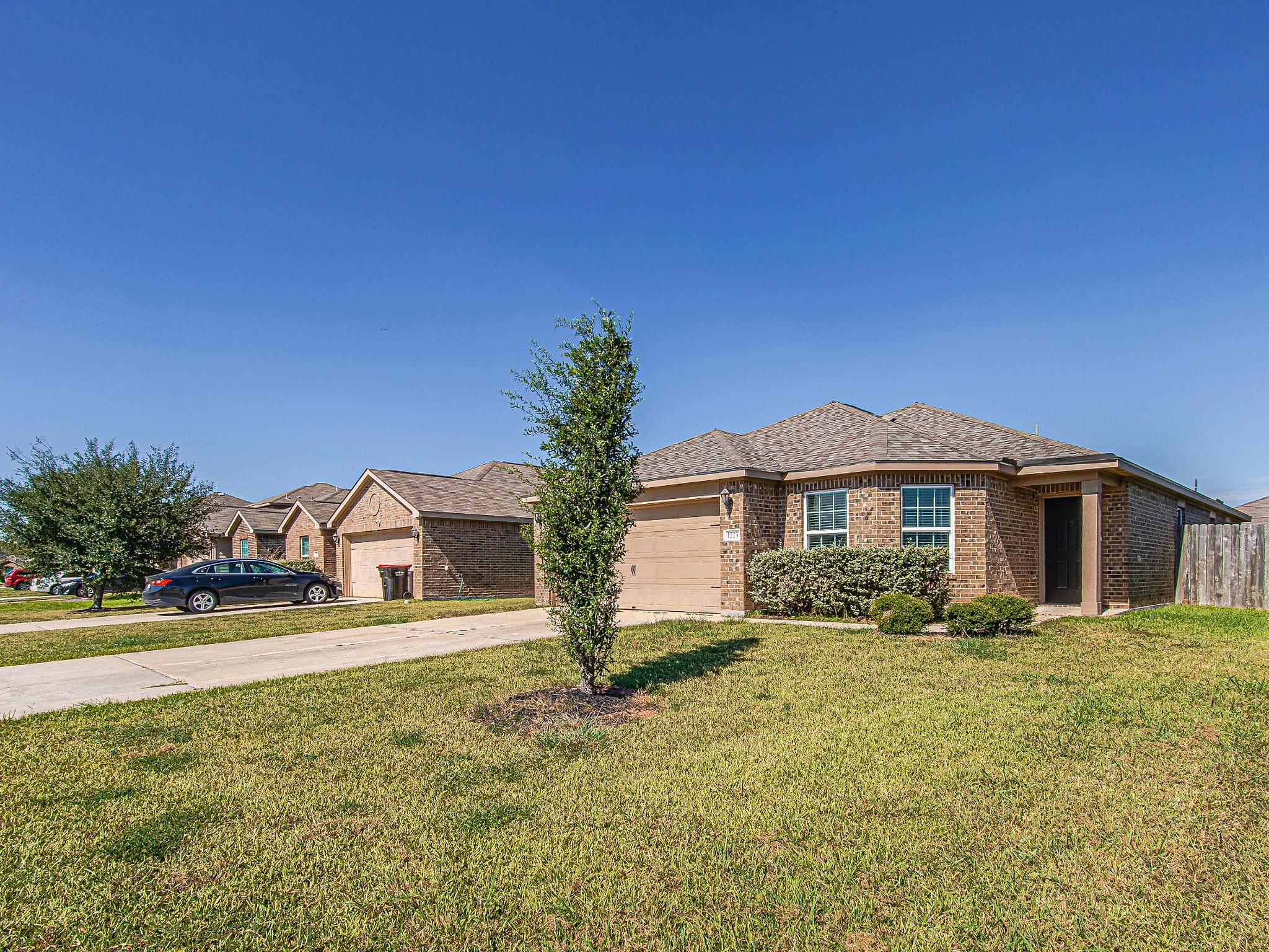 An alternate front view highlights the brick exterior, landscaped planting beds, and walkway leading to the covered entrance.