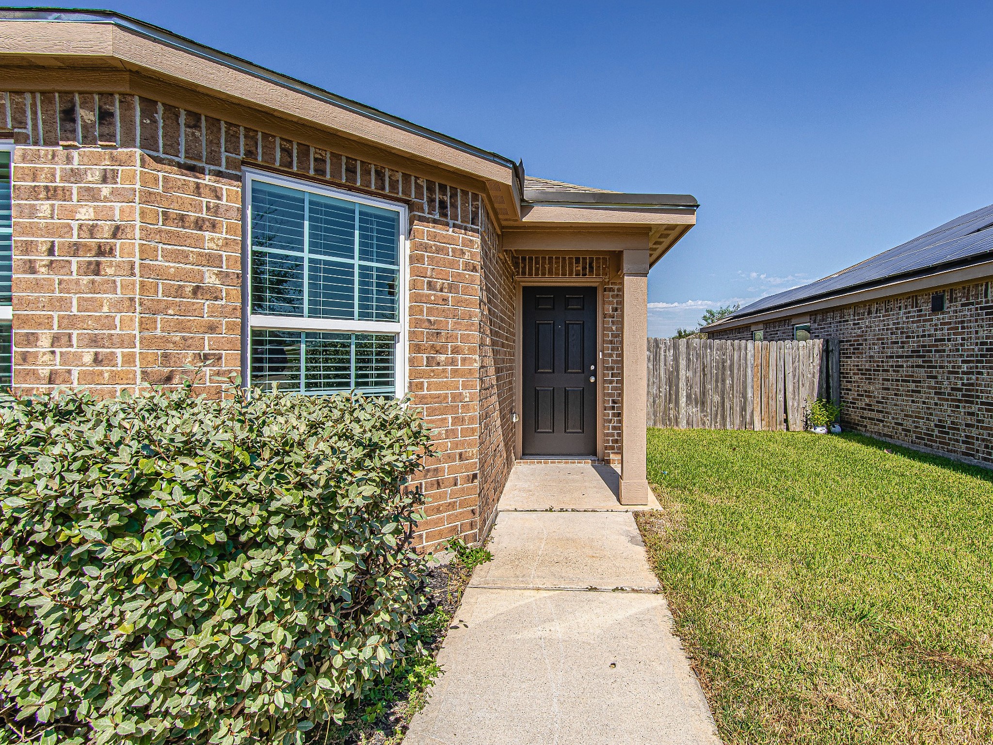 A covered front entry welcomes guests, with a concrete walkway and established shrubs framing the approach.