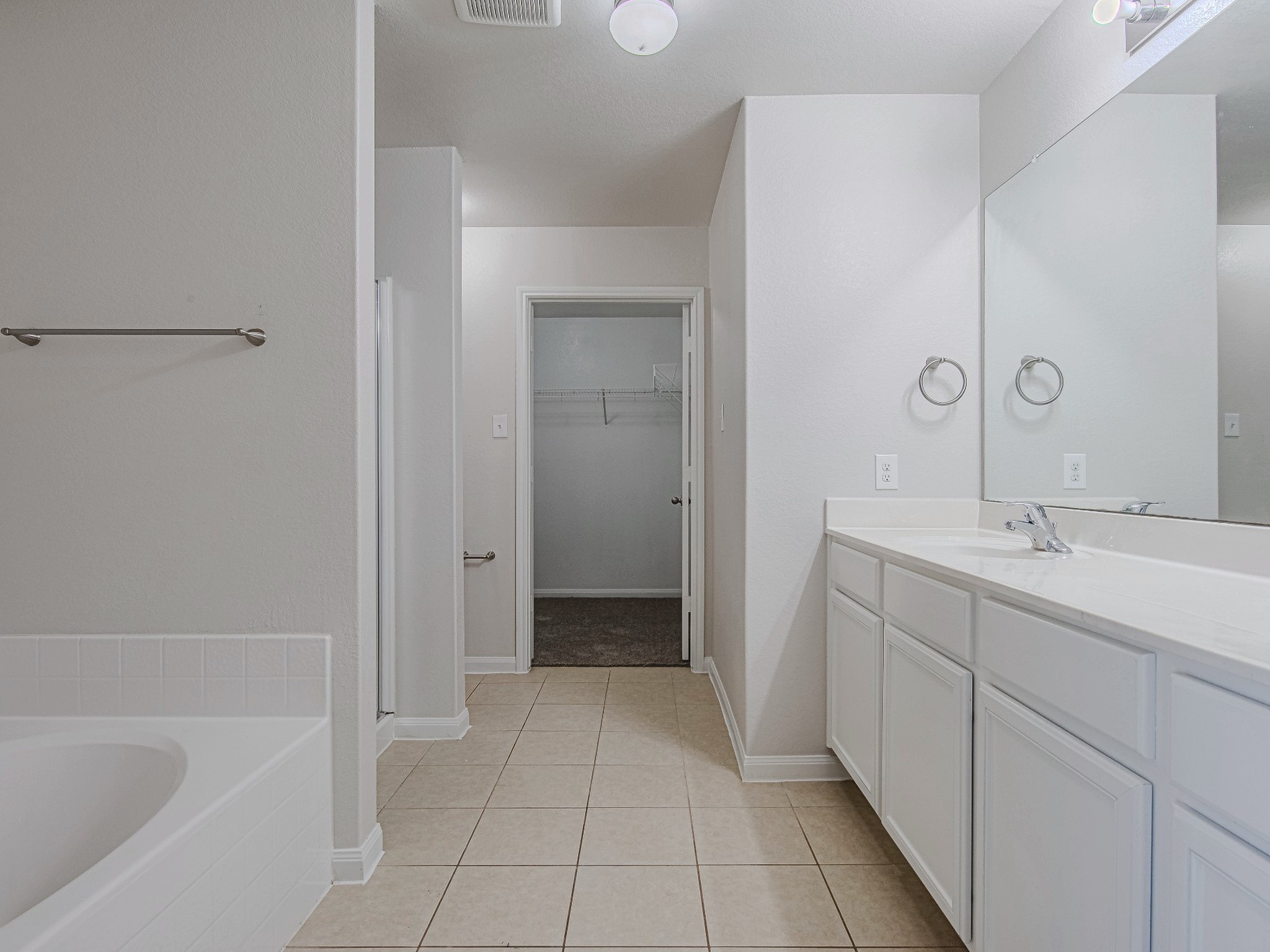 The primary bathroom features a long vanity with cabinet storage, tile flooring, and a separate tub and shower.