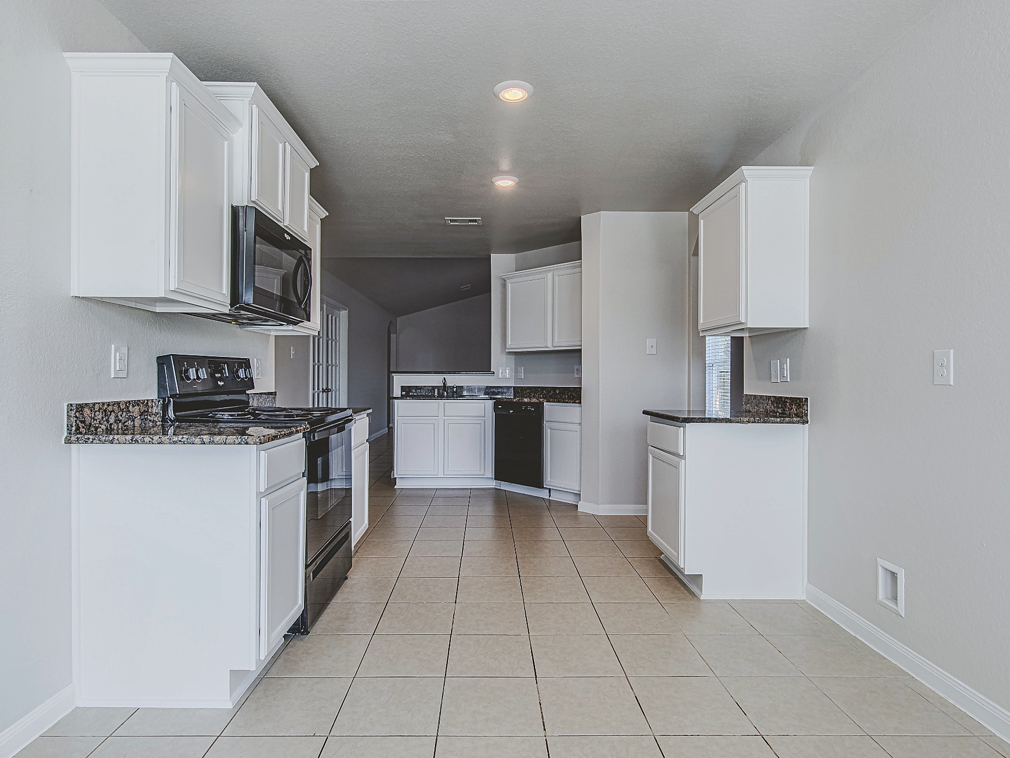 This alternate kitchen view showcases the white cabinetry, contrasting granite countertops, and tile flooring carried throughout the space.