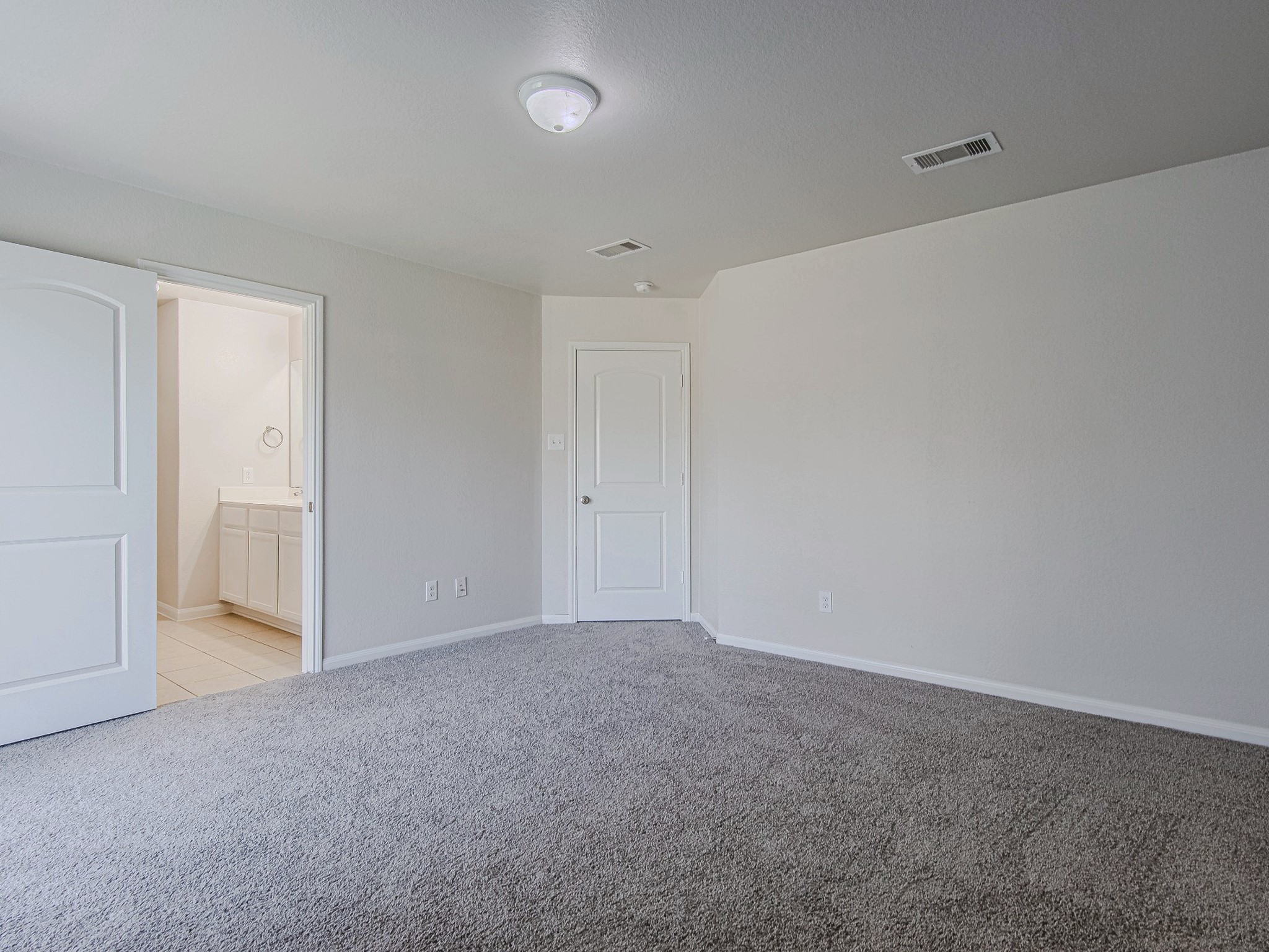 An alternate view of the primary bedroom highlights its neutral palette and direct access to the adjoining bathroom.