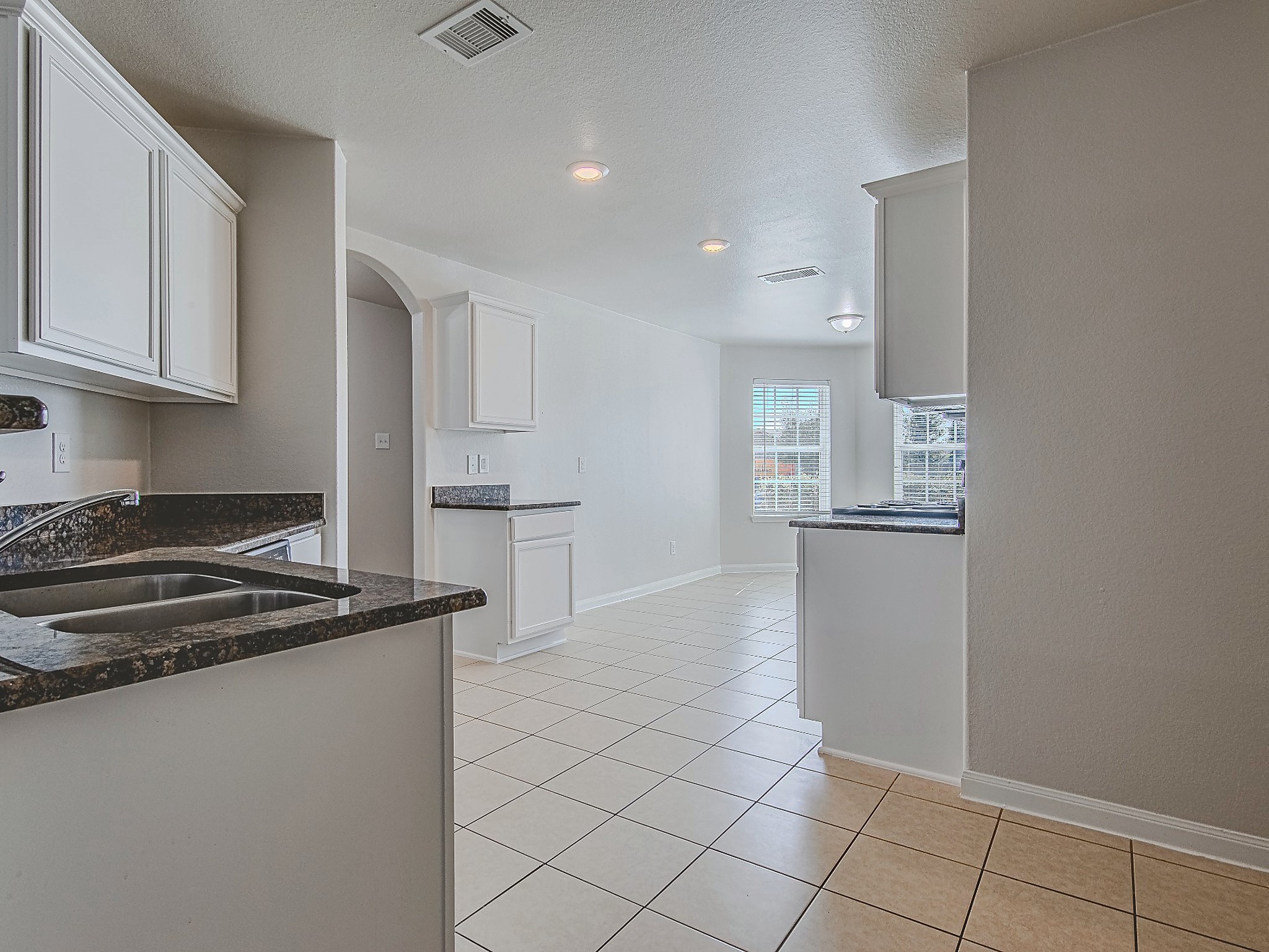 The kitchen features granite countertops, white cabinetry, and tile flooring, with a bright dining nook just beyond.