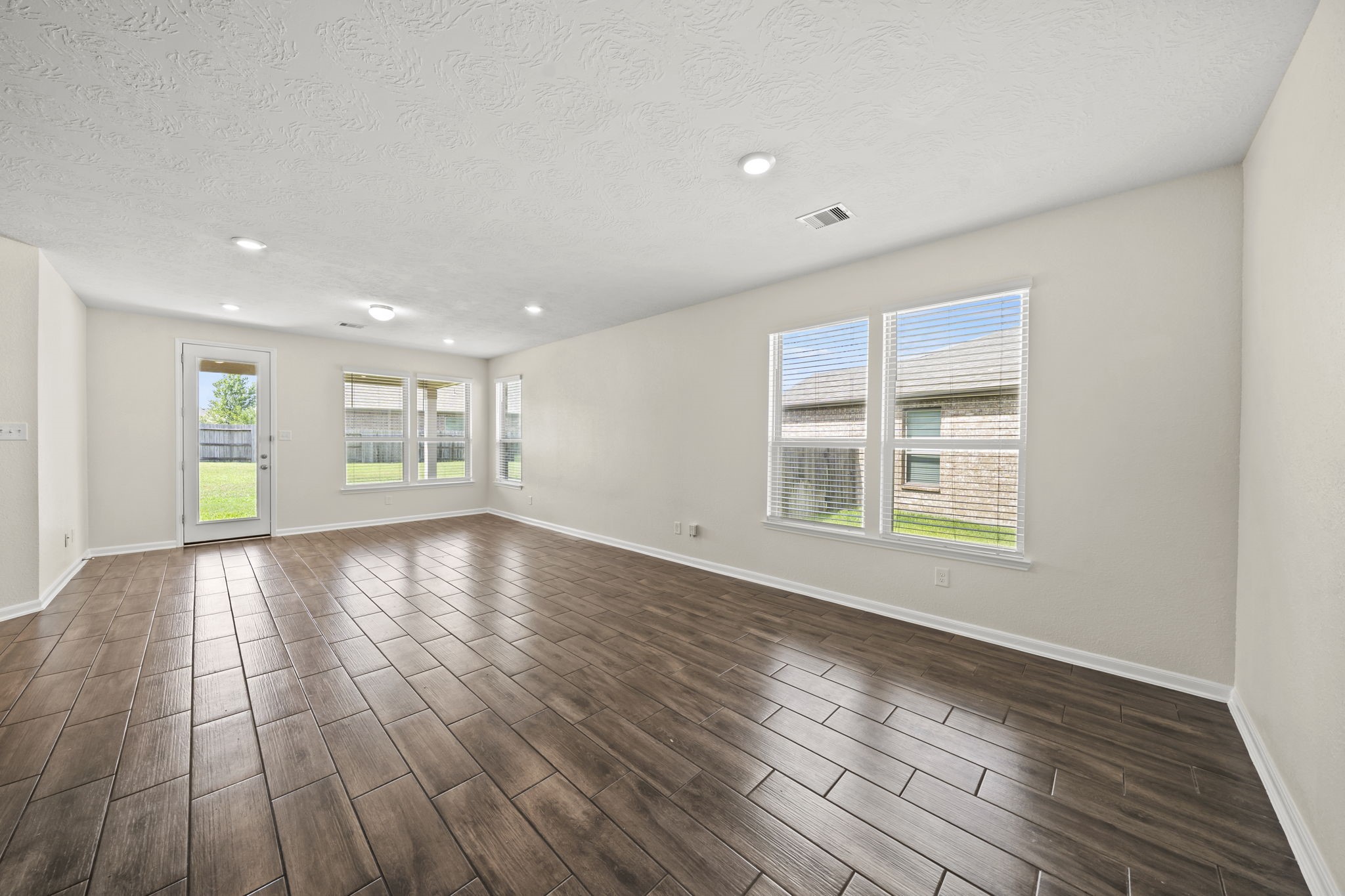 Spacious main living area featuring rich wood-look tile flooring. Flooded with natural light from large windows, this open layout offers seamless connectivity to the backyard patio.