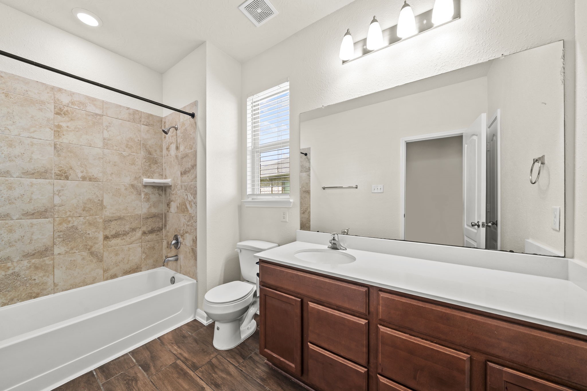 Full secondary bath offering a extended single-sink vanity, wood cabinetry, and wood-look tile flooring.