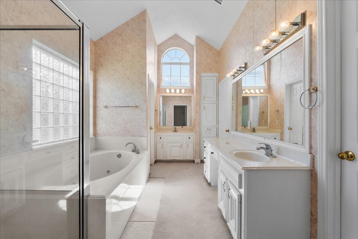 Soaring vaulted ceilings and a dramatic arched transom window bathe this primary en-suite in bright, refreshing natural light.