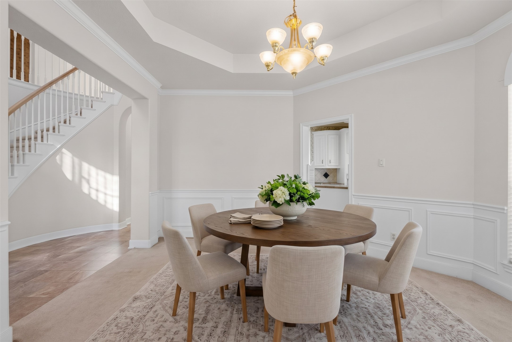 Refined dining space showcasing detailed wall trim, decorative sunburst window transoms, a central chandelier, and convenient swinging-door access to the kitchen.