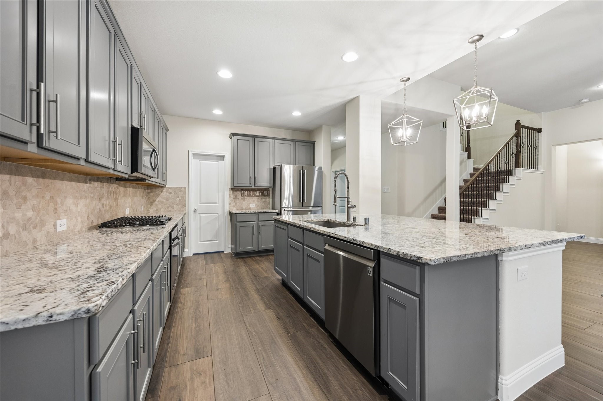 Stunning kitchen that  features extensive gray cabinetry, granite countertops, stainless steel appliances, and a large center island with an undermount sink and seating area.