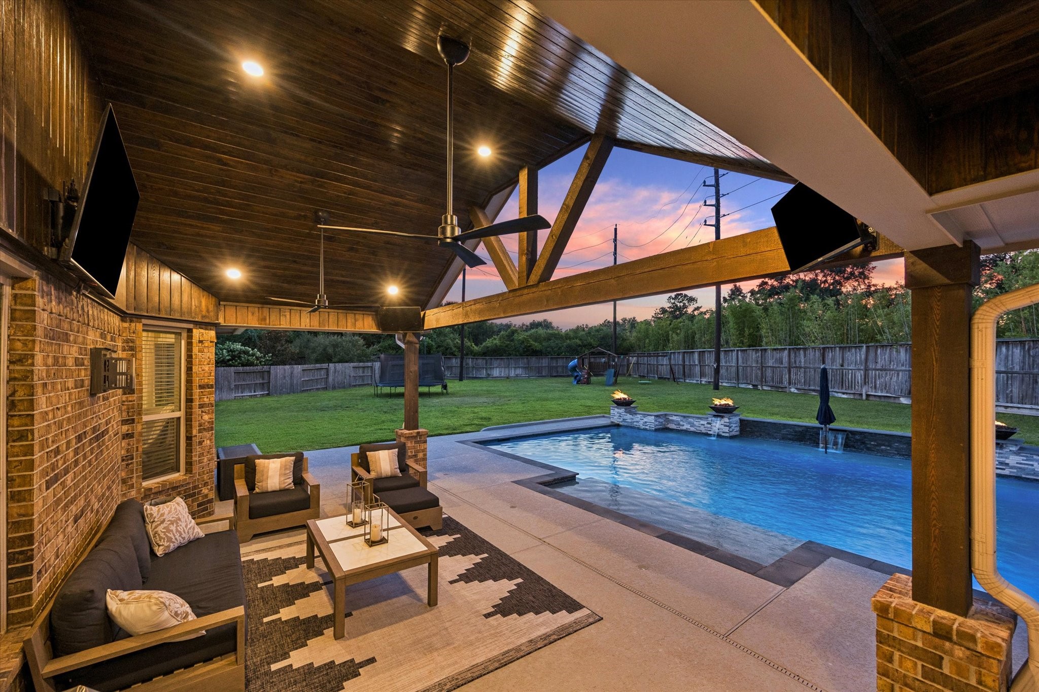 Designed for effortless indoor-outdoor living, this spectacular covered patio creates a true private retreat overlooking the resort-style pool. Rich wood-paneled ceilings, exposed beams, and warm recessed lighting bring a sophisticated lodge-inspired character to the space, while comfortable lounge seating provides the perfect setting for relaxing or entertaining.