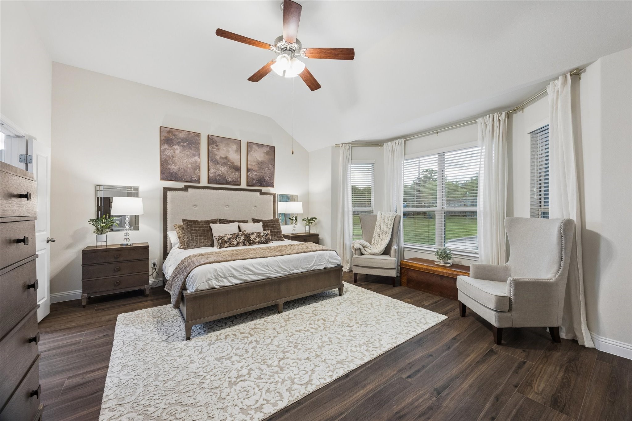 Serene primary bedroom featuring a vaulted ceiling, a wall of large windows that fills the room with light and offers peaceful backyard views!